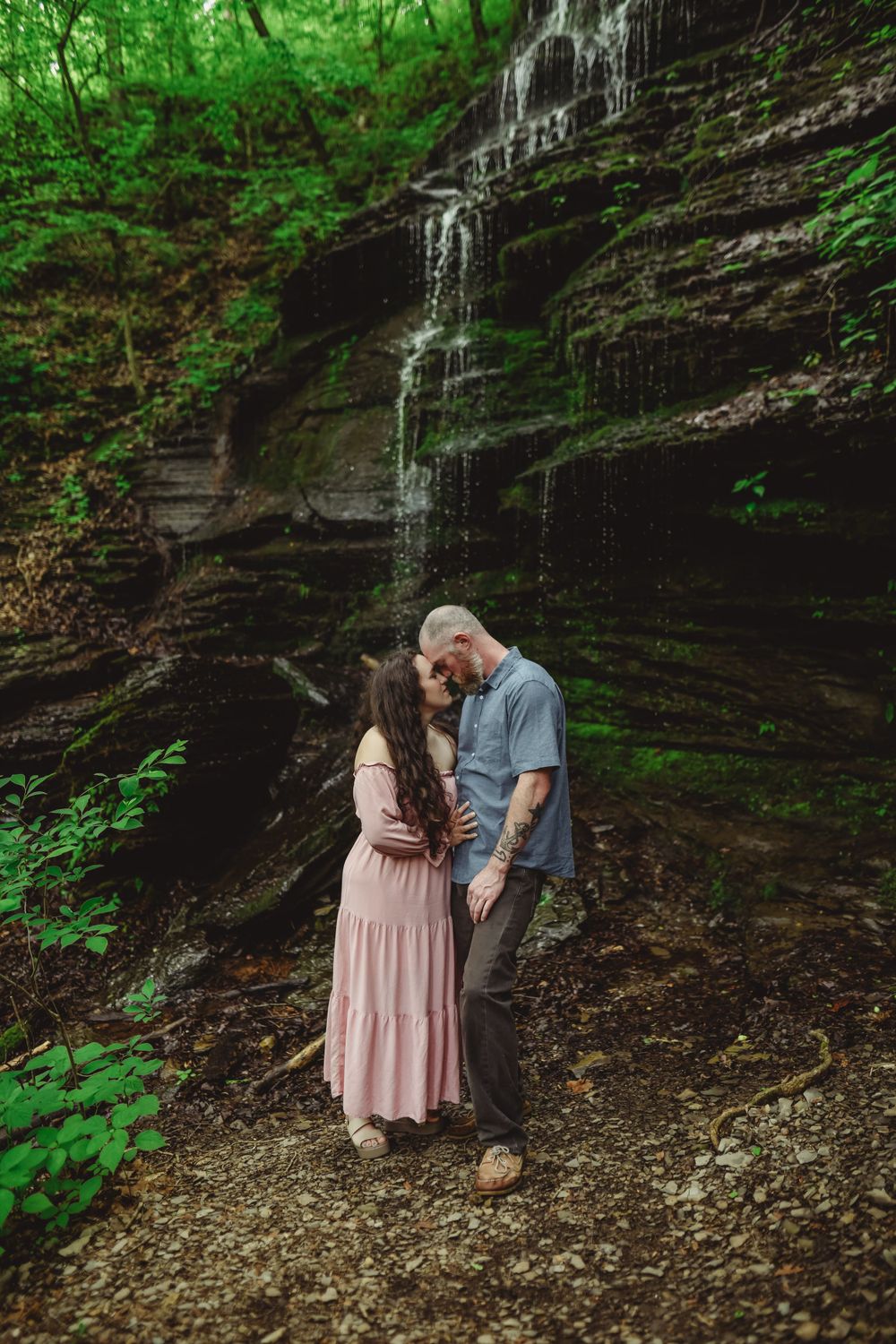 A tender moment captured by a rocky waterfall wall in a forest setting.