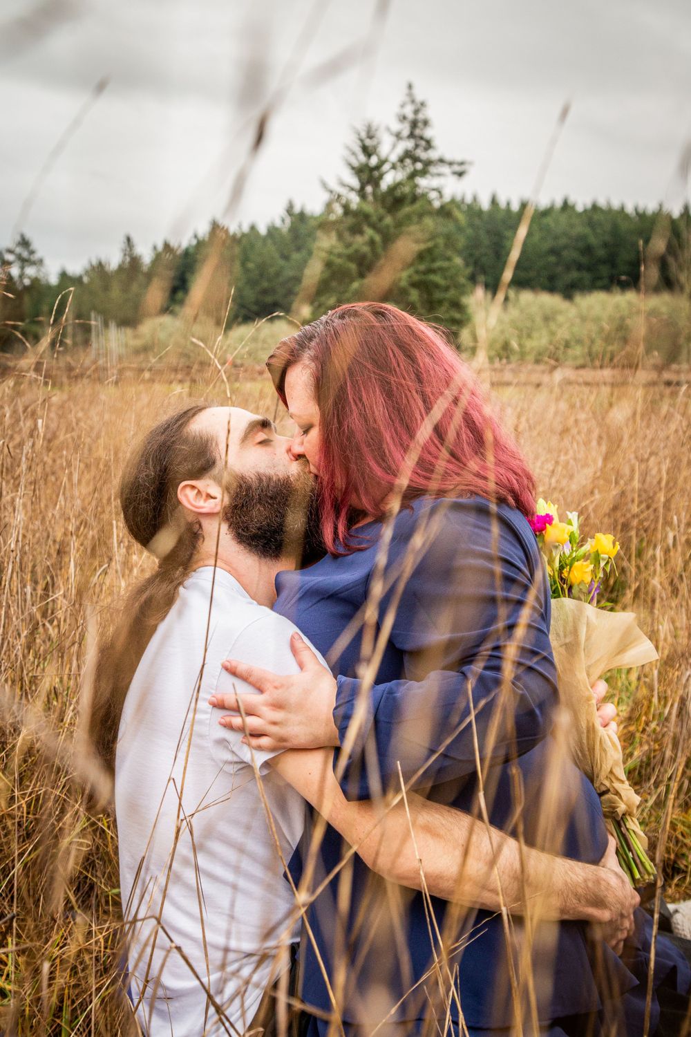 Two people embracing passionately amidst tall wheat grass with yellow flowers.