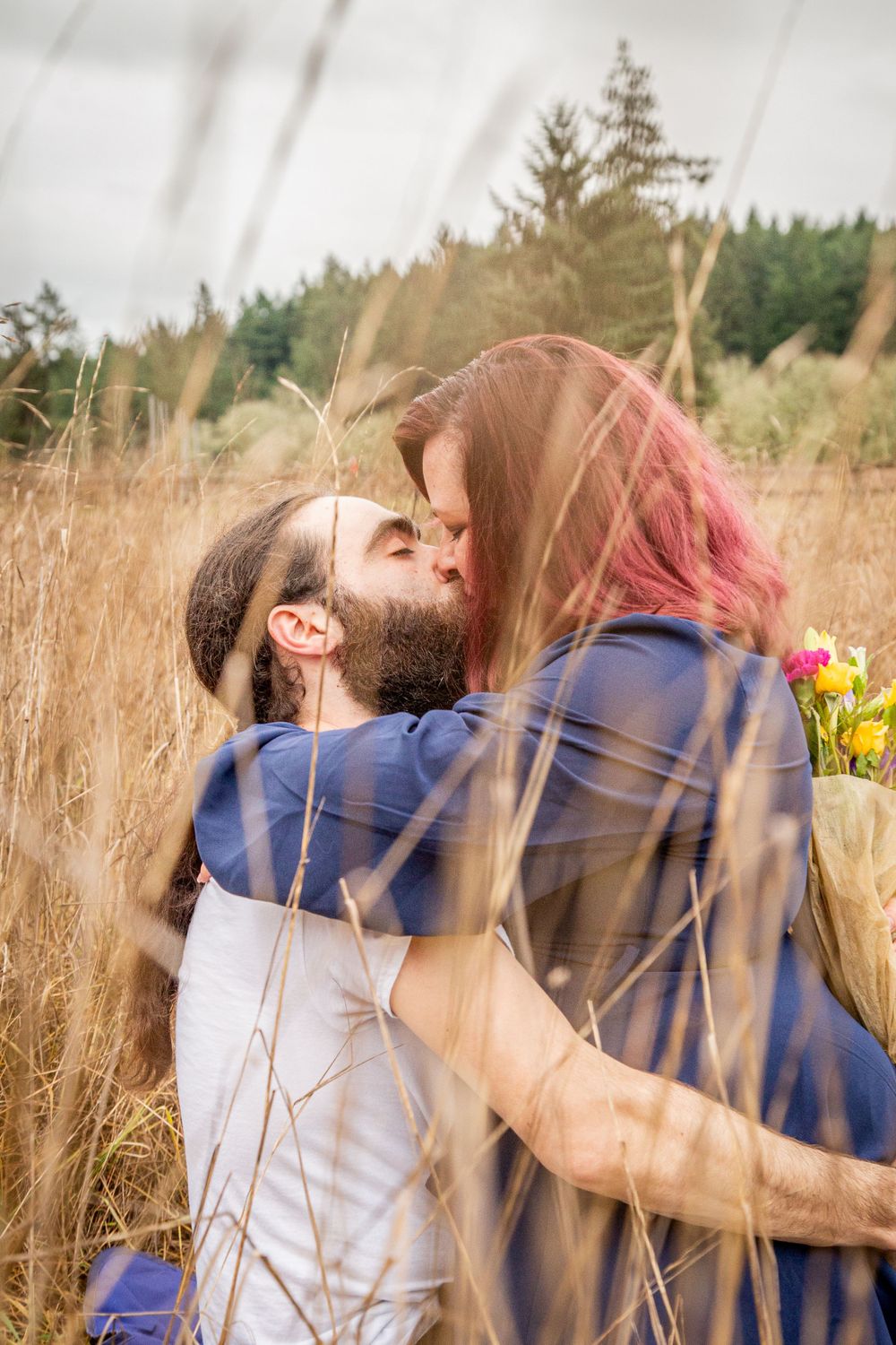 A romantic embrace captured in a sunlit field of tall grass and evergreen trees.