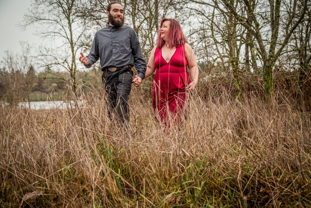 A couple walks through tall grass while dressed in contrasting red and dark outfits.