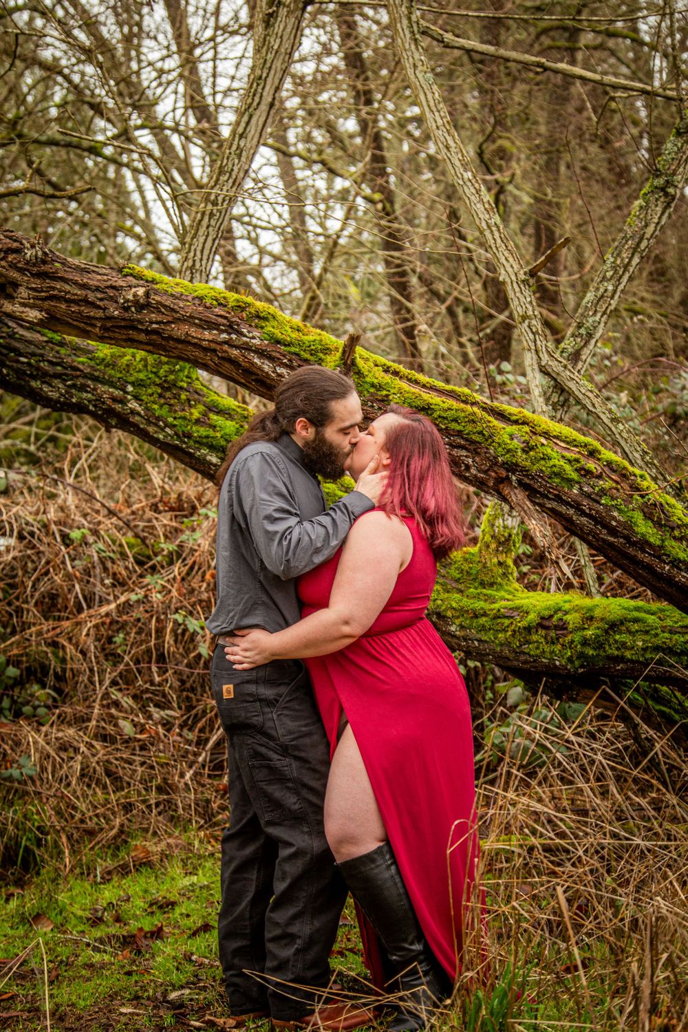 A romantic embrace by a moss-covered log in a natural forest setting.