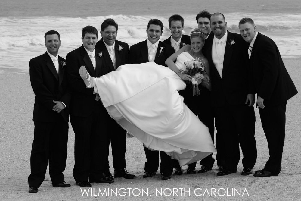 Wedding party poses on beach in Wilmington North Carolina as groomsmen hold bride in flowing white dress.