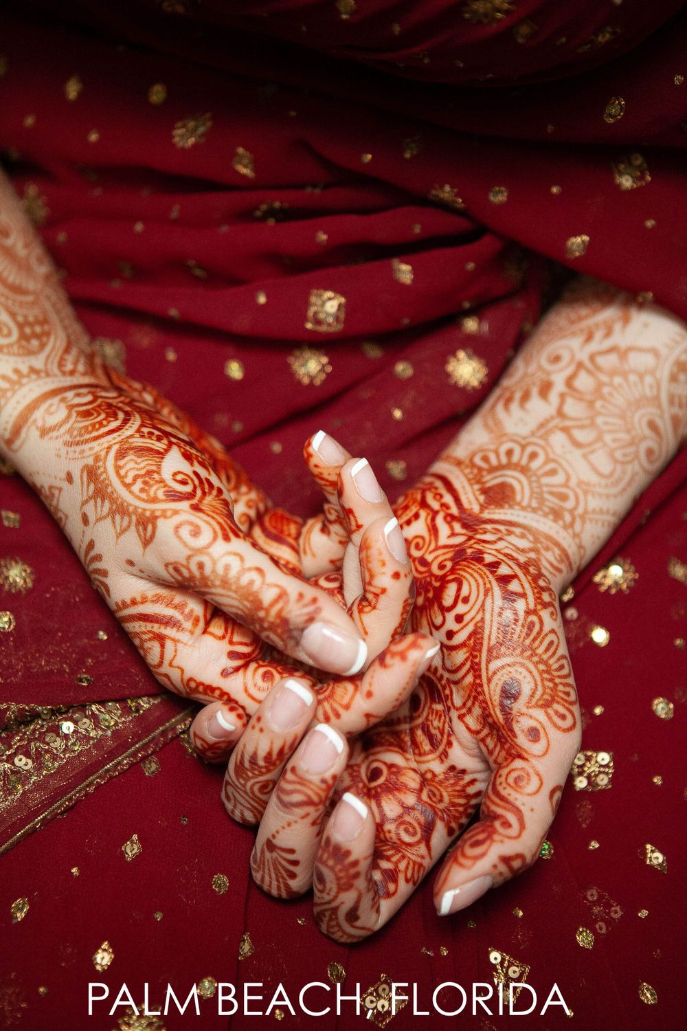 Intricate henna mehndi designs adorning hands resting on red fabric with gold embellishments in Palm Beach, Florida.