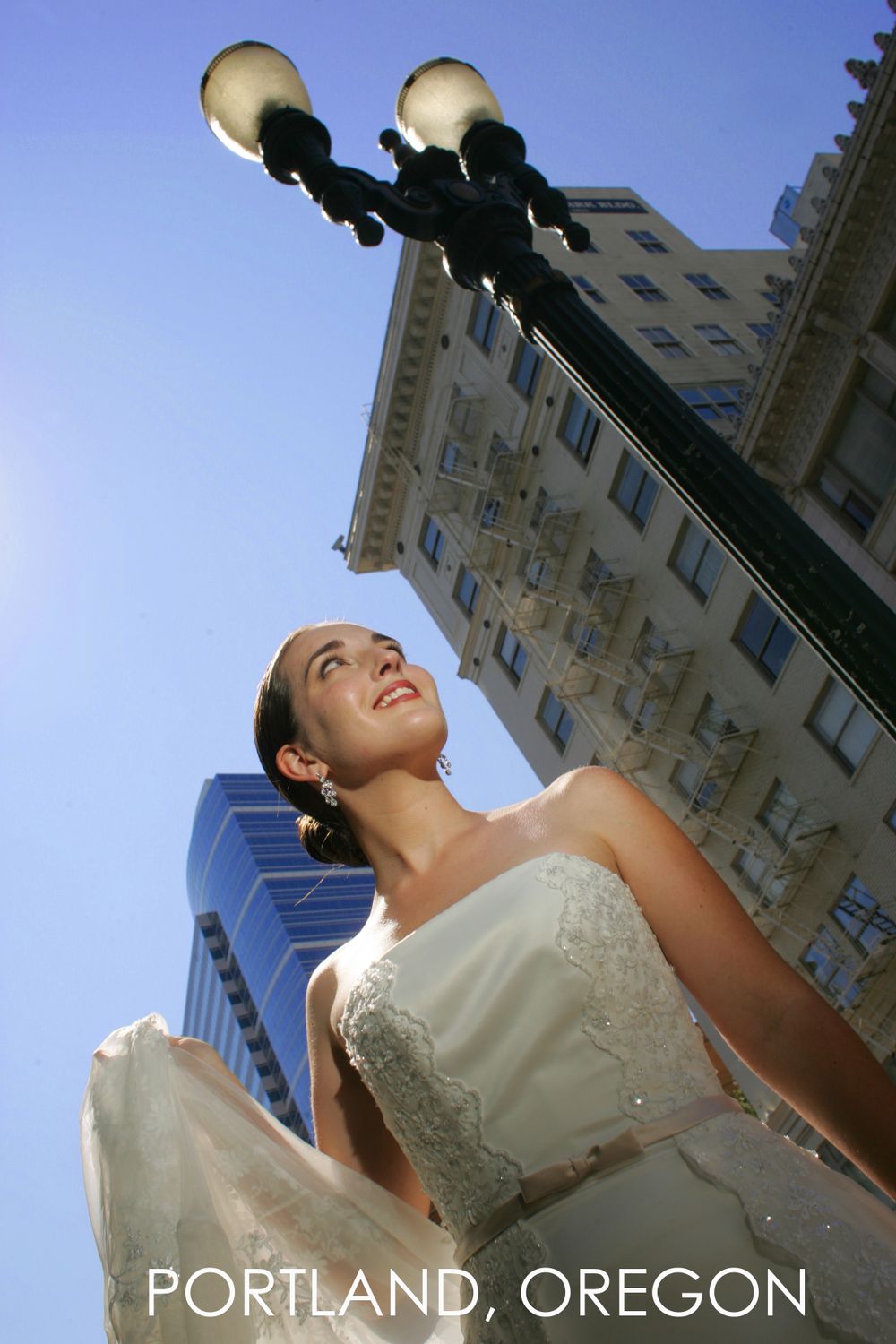 Upward view of bride in white dress against urban architecture and vintage lamp post in Portland.
