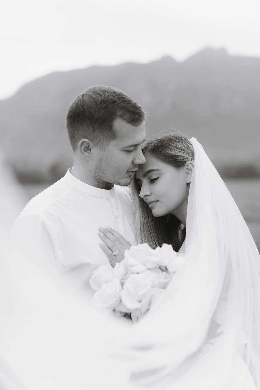 A tender black and white wedding portrait with mountains creating a dramatic backdrop.