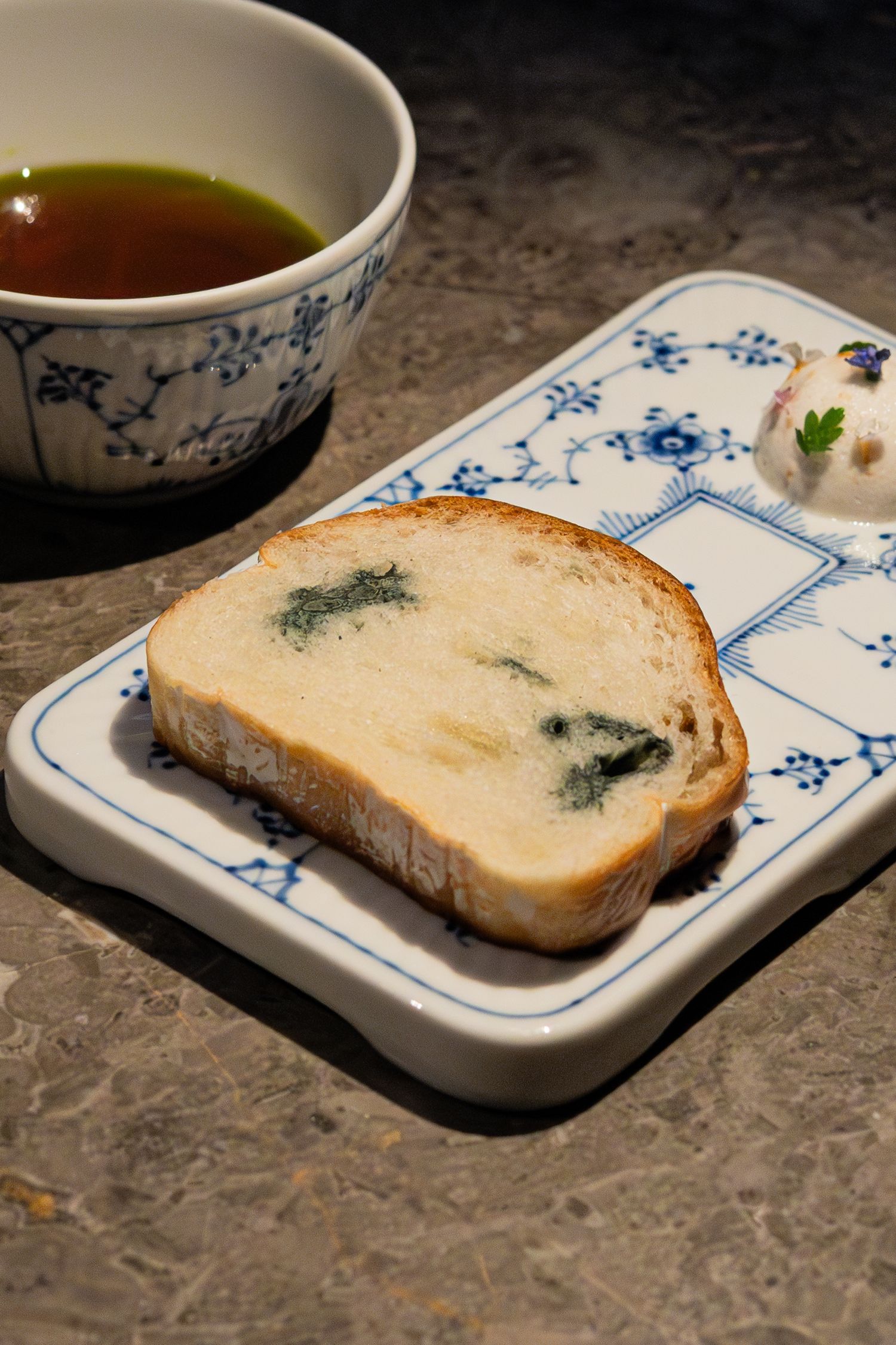 Slice of bread with green herbs served with tea in blue and white porcelain dishware.