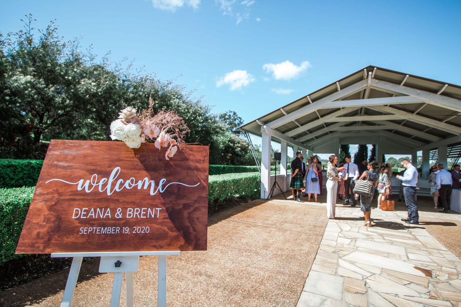 Outdoor wedding venue with wooden welcome sign and white tent structure.