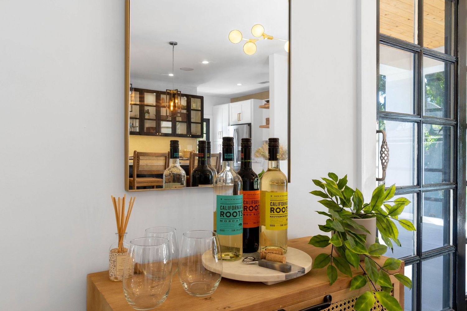 Bar area with glass bottles, cocktail glasses, and decorative plant on wooden table.