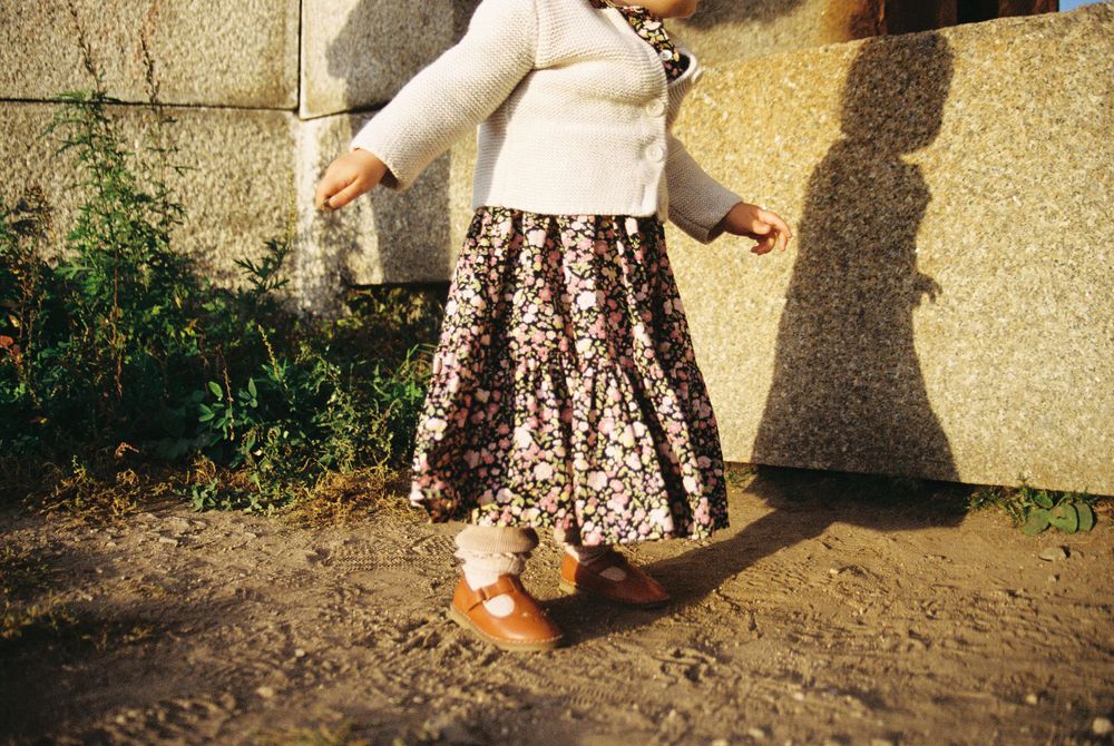 Person wearing a floral dress casting shadow on wall while walking outdoors.