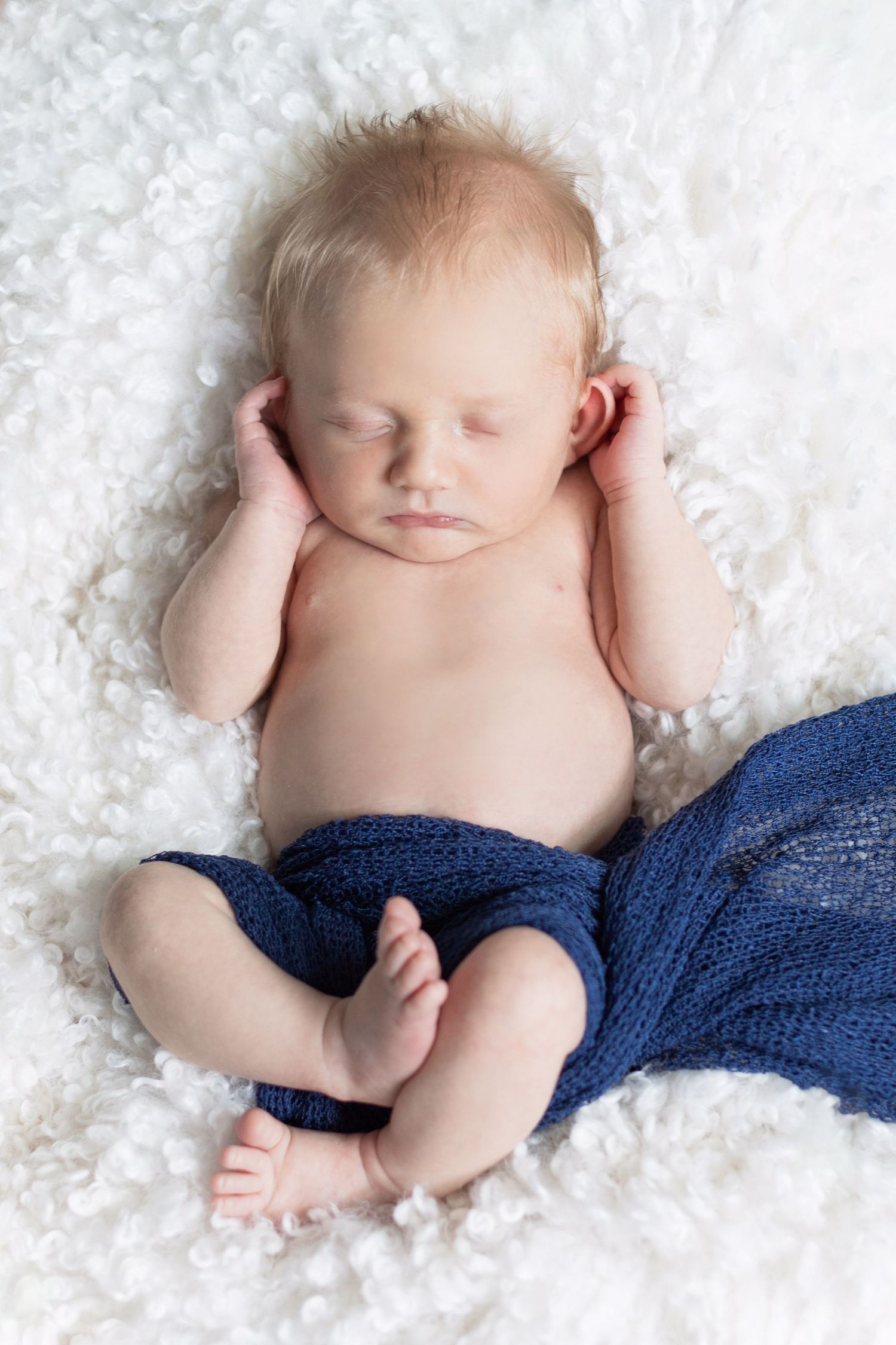 Newborn baby sleeping on white textured blanket with navy blue wrap.