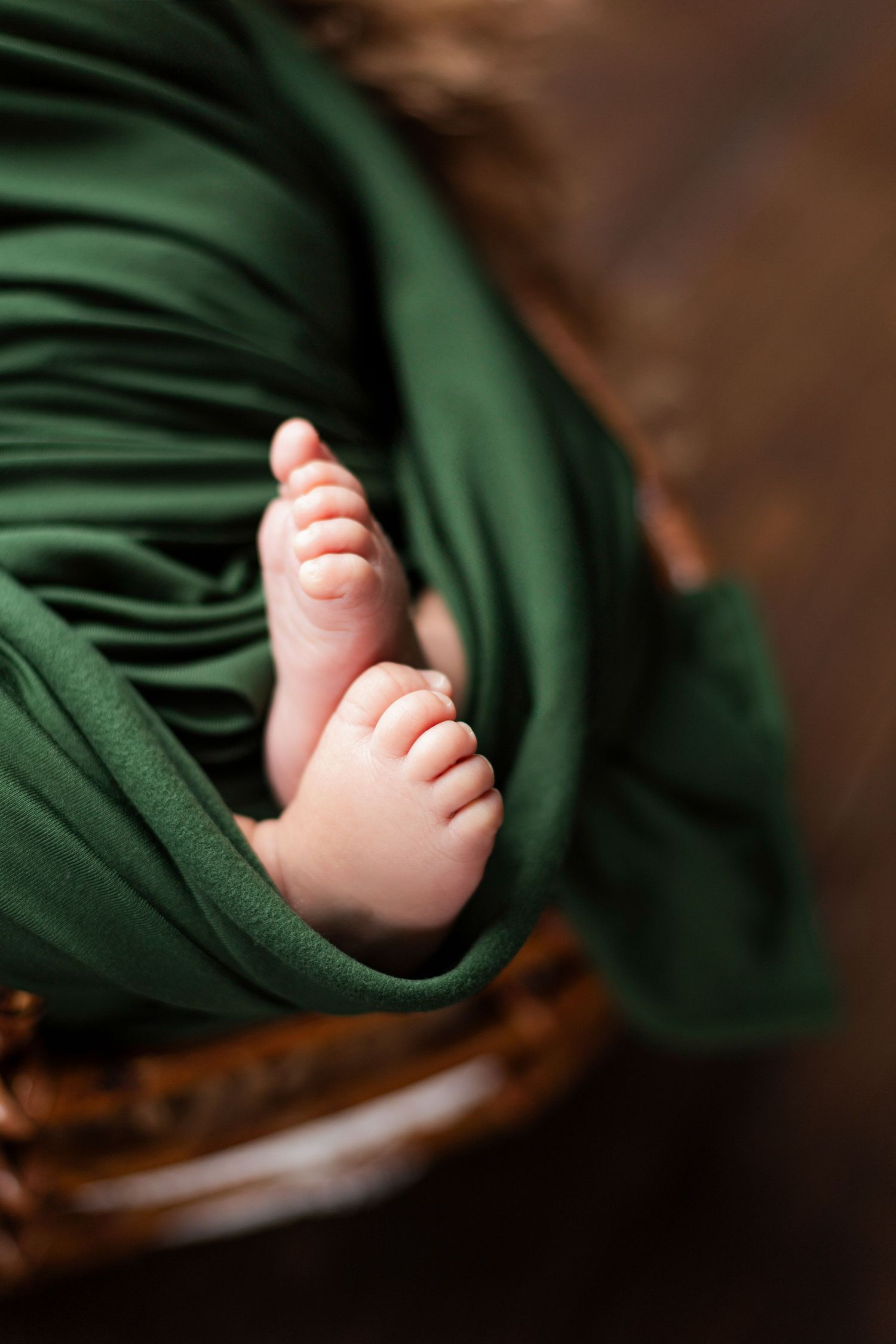 Close-up series of tiny baby feet wrapped in dark green blanket against wooden background.