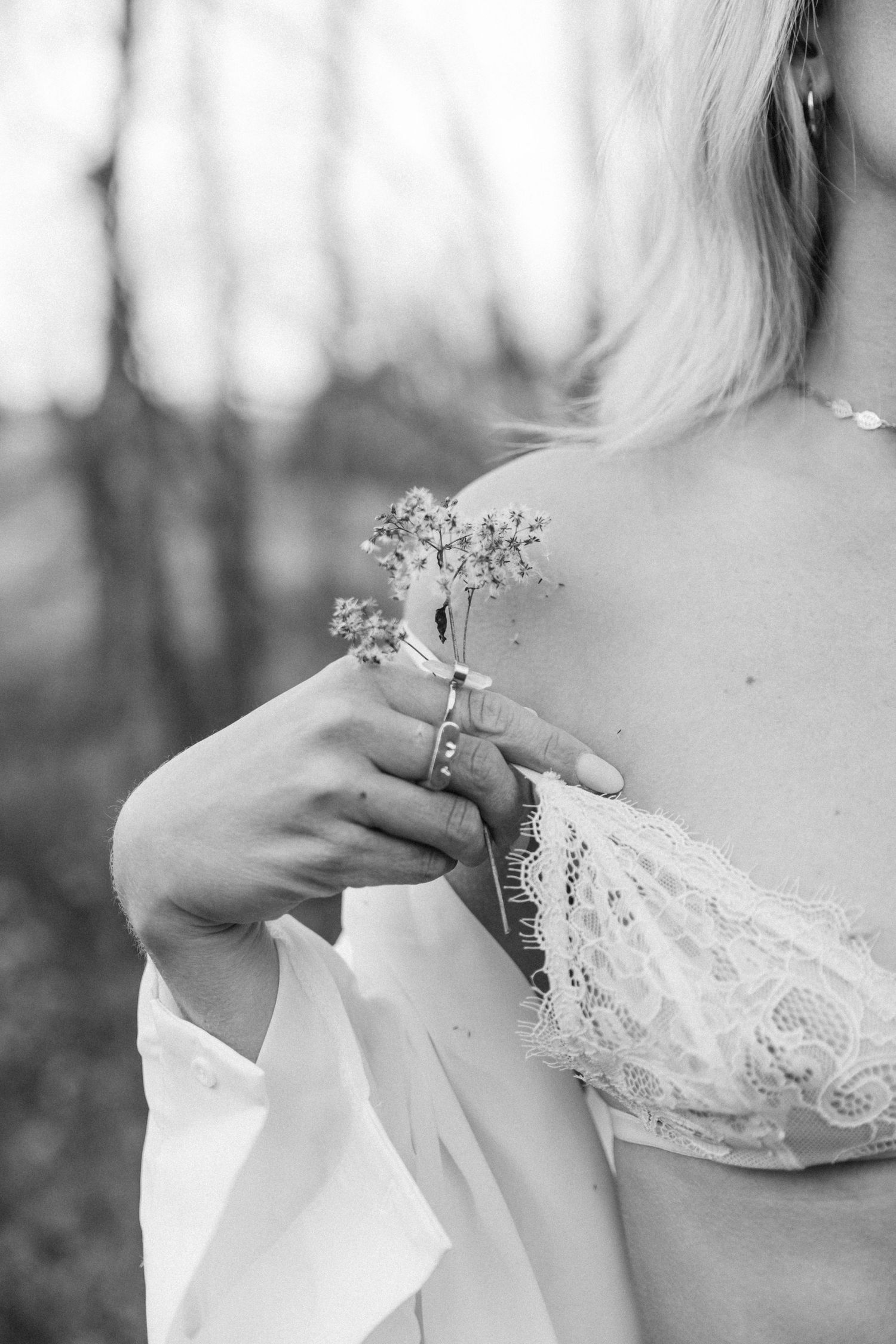 A dreamy black and white photo series showing delicate lace details of a wedding dress against a blurred forest backdrop.