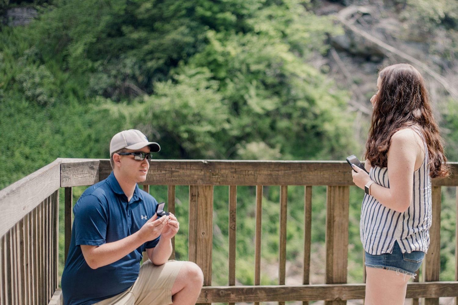 A couple sharing a special moment on a wooden deck overlooking a scenic waterfall in the mountains.