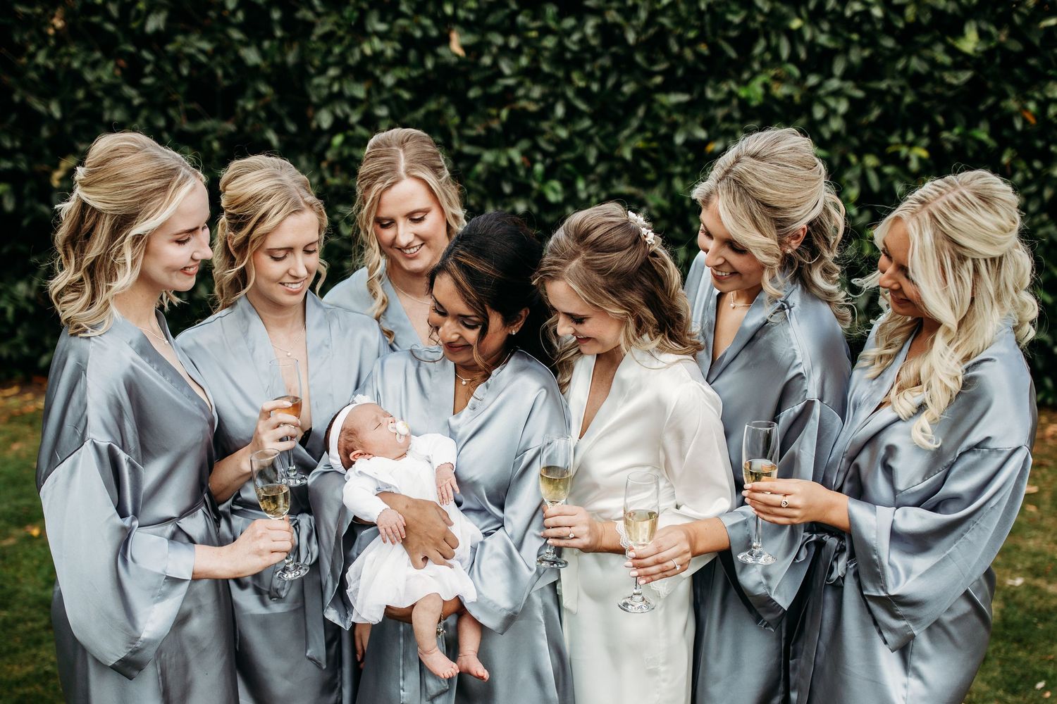 Bridal party in matching grey robes gather together in a garden setting.