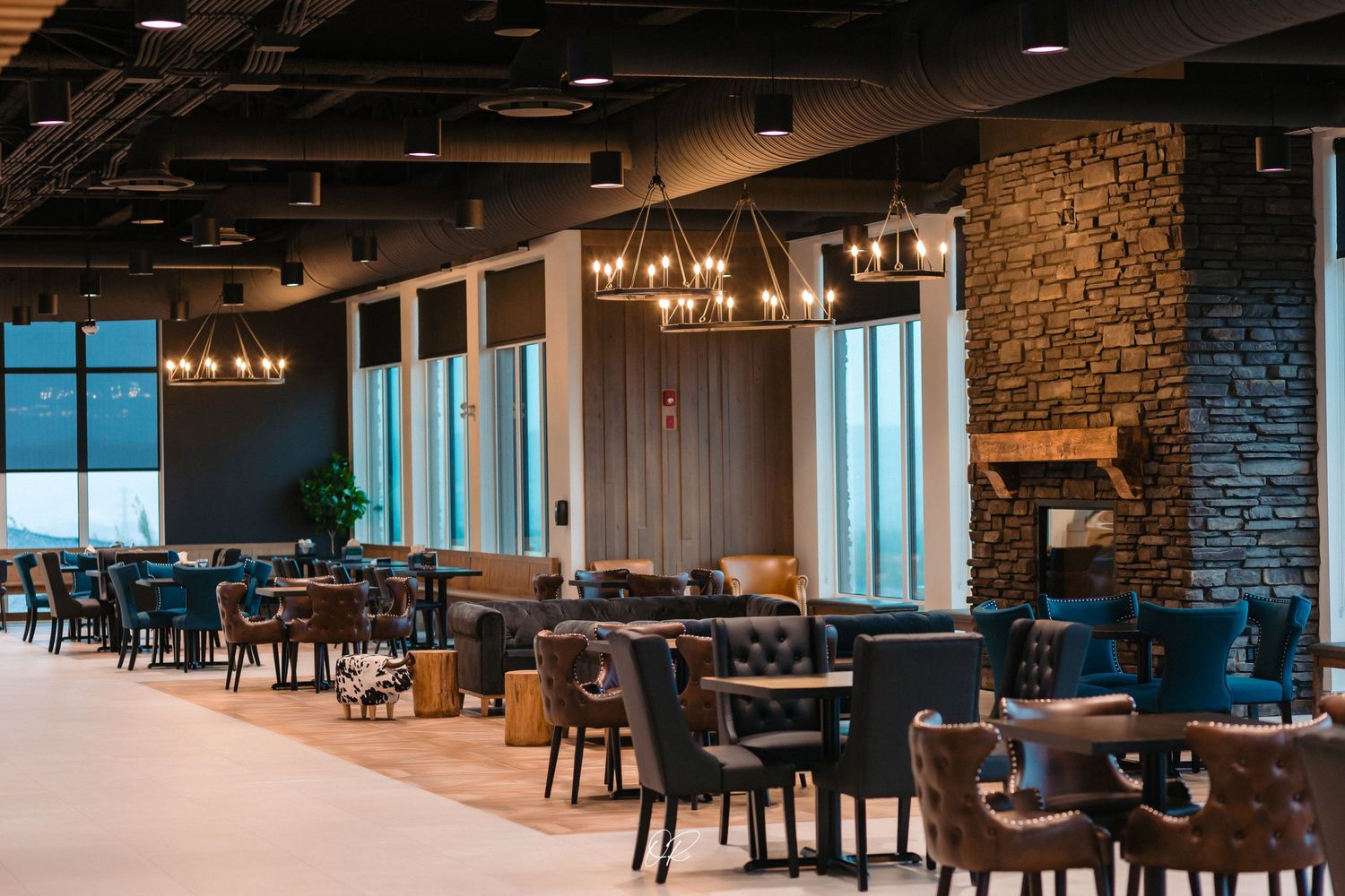 Modern restaurant interior with stone walls, chandeliers, and blue chairs in an elegant dining setup.