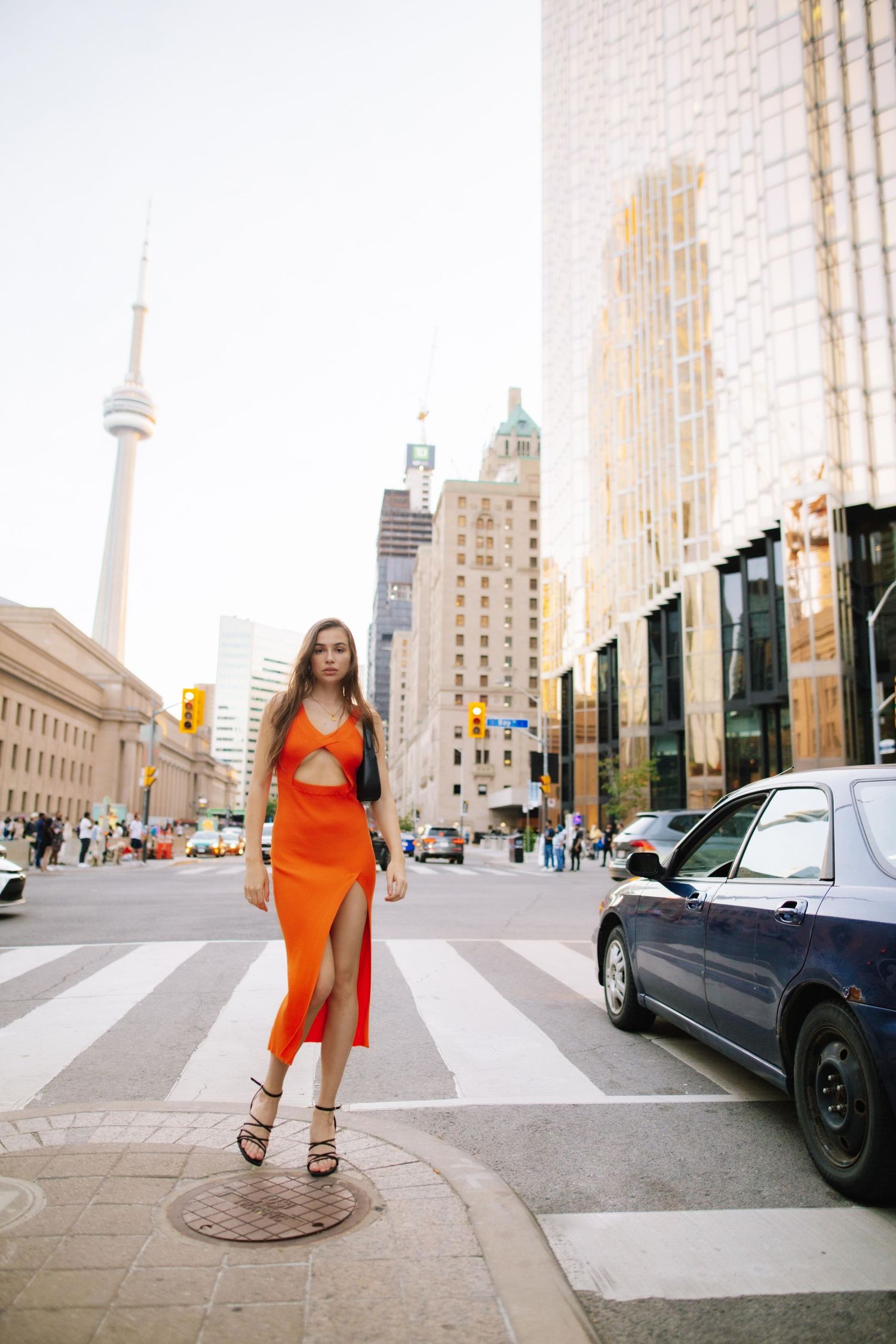 Street scene in Toronto with CN Tower and person in orange dress crossing crosswalk.