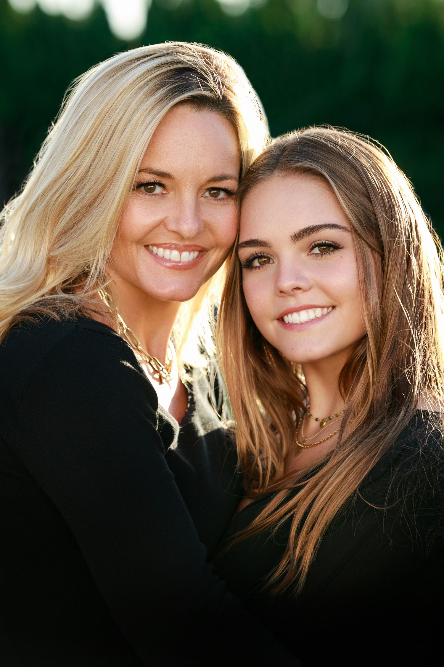 Two people in black tops share an intimate portrait moment in golden outdoor lighting.