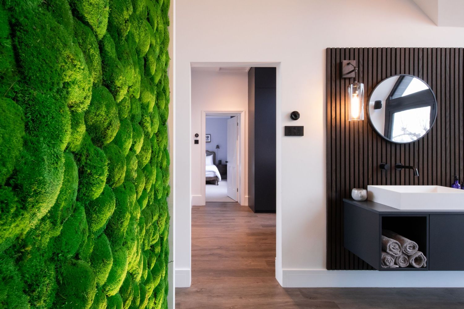 Modern bathroom interior design featuring a moss wall, round mirror, and wood accents with minimalist styling.