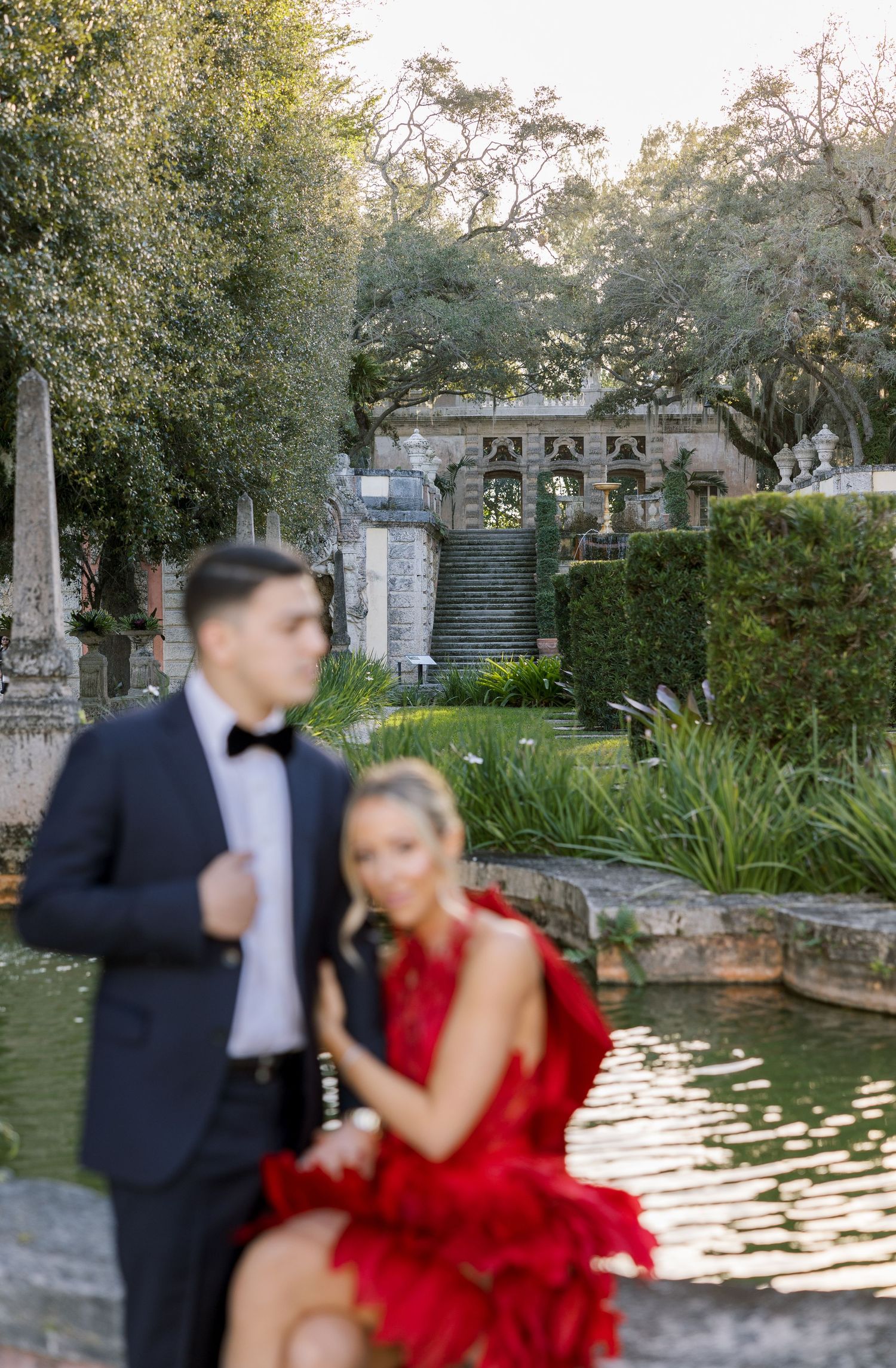 Romantic portrait by a garden pond with classical architecture in background.