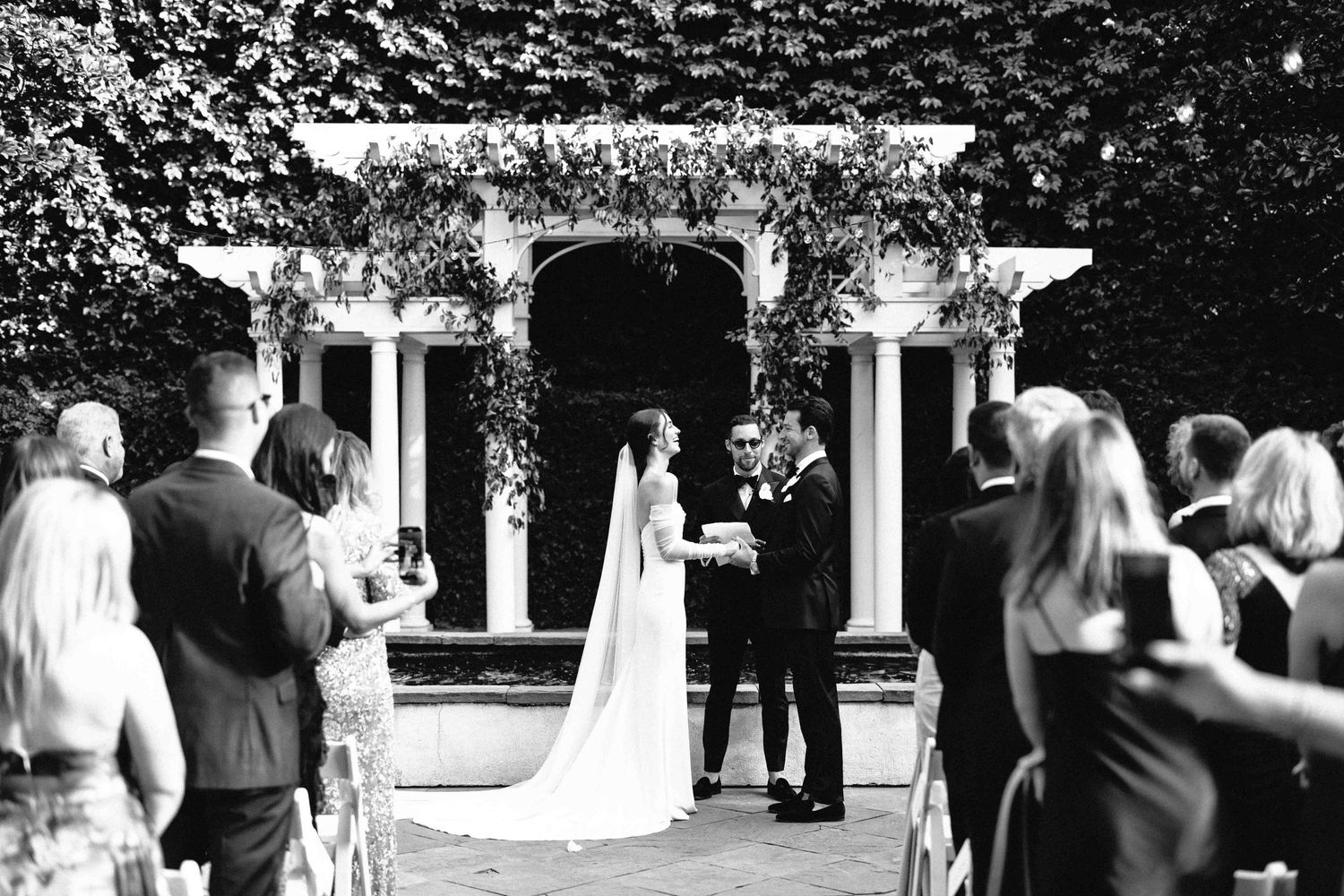 Emotional black and white image of an elegant couple holding hands, smiling during a William Aiken House wedding ceremony, in Charleston,SC