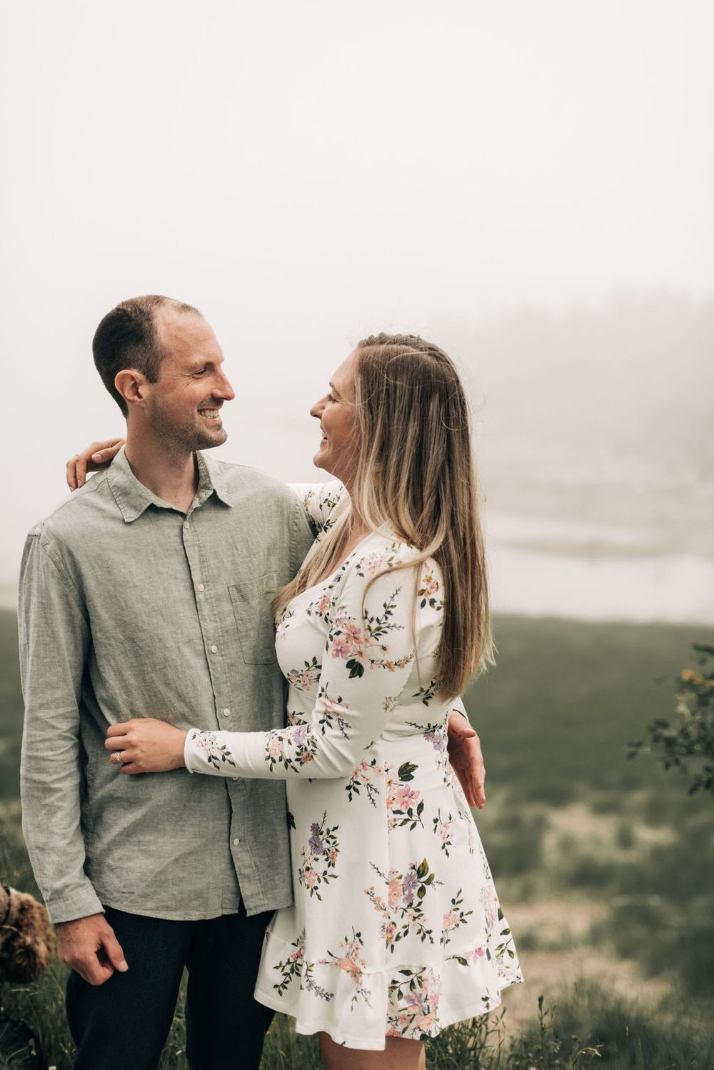 A couple embraces on a misty hilltop wearing casual attire while sharing an intimate moment.