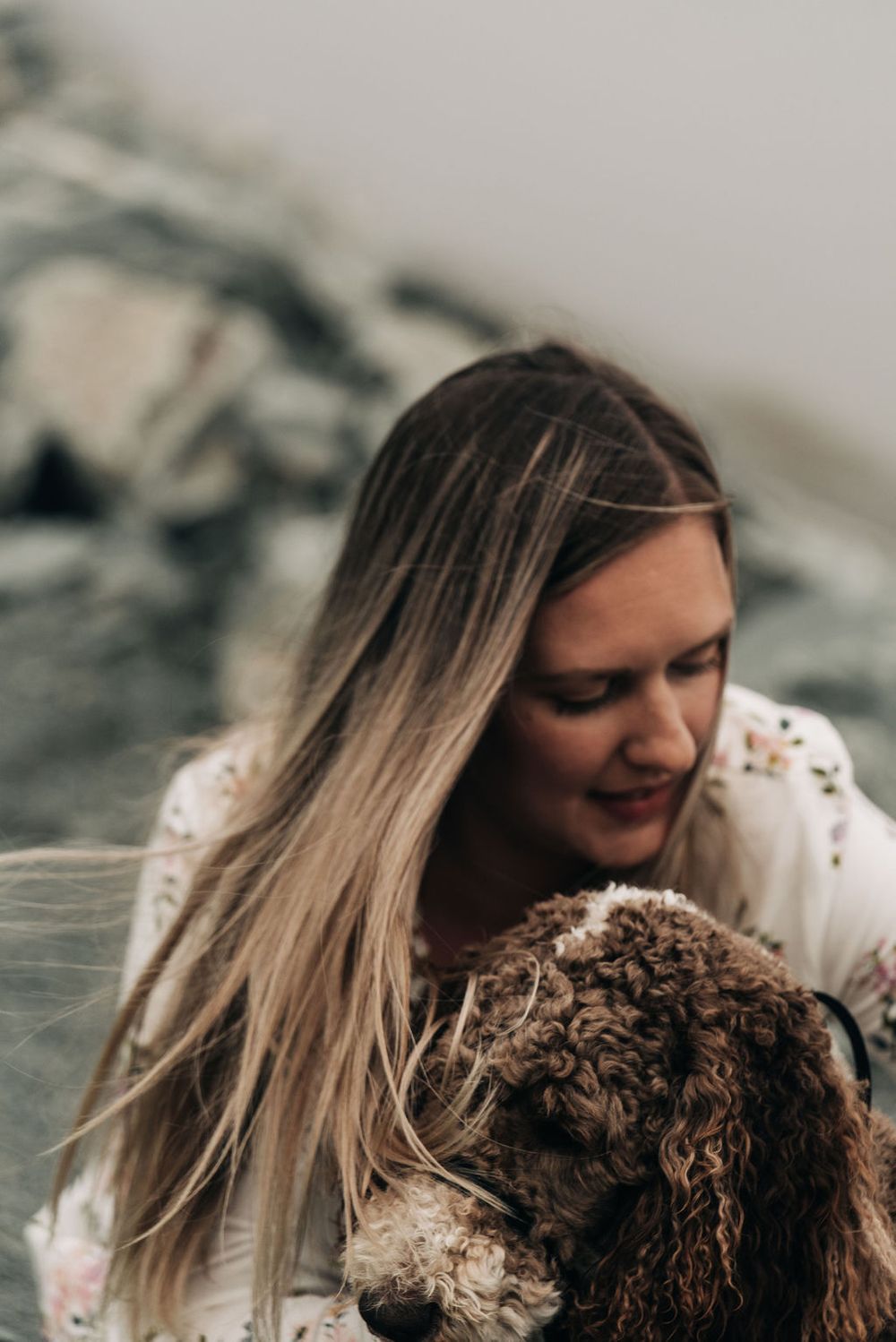 Person with long blonde hair cuddling with a brown curly-haired dog.