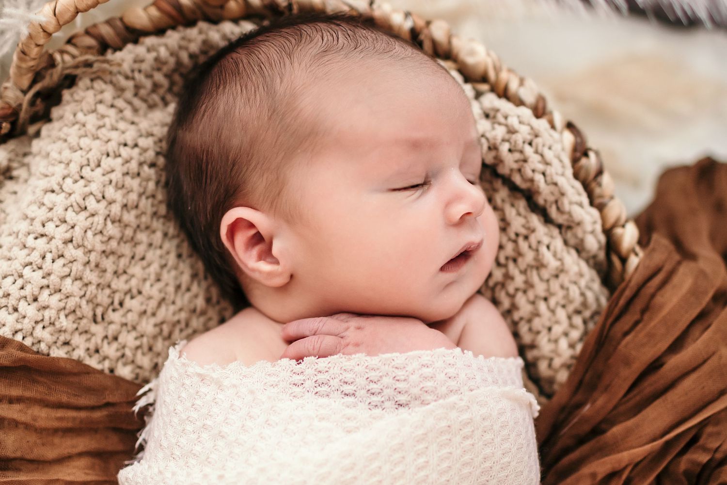 a newborn baby lays in a basket with his eyes closed and swaddled while posing for a photo
