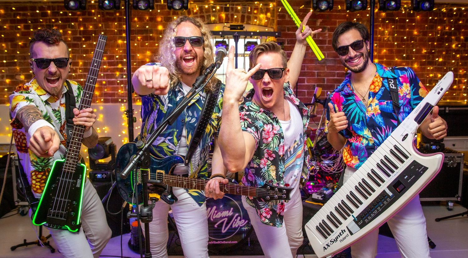 A colorful retro band in wild outfits poses with instruments against a sparkly backdrop.