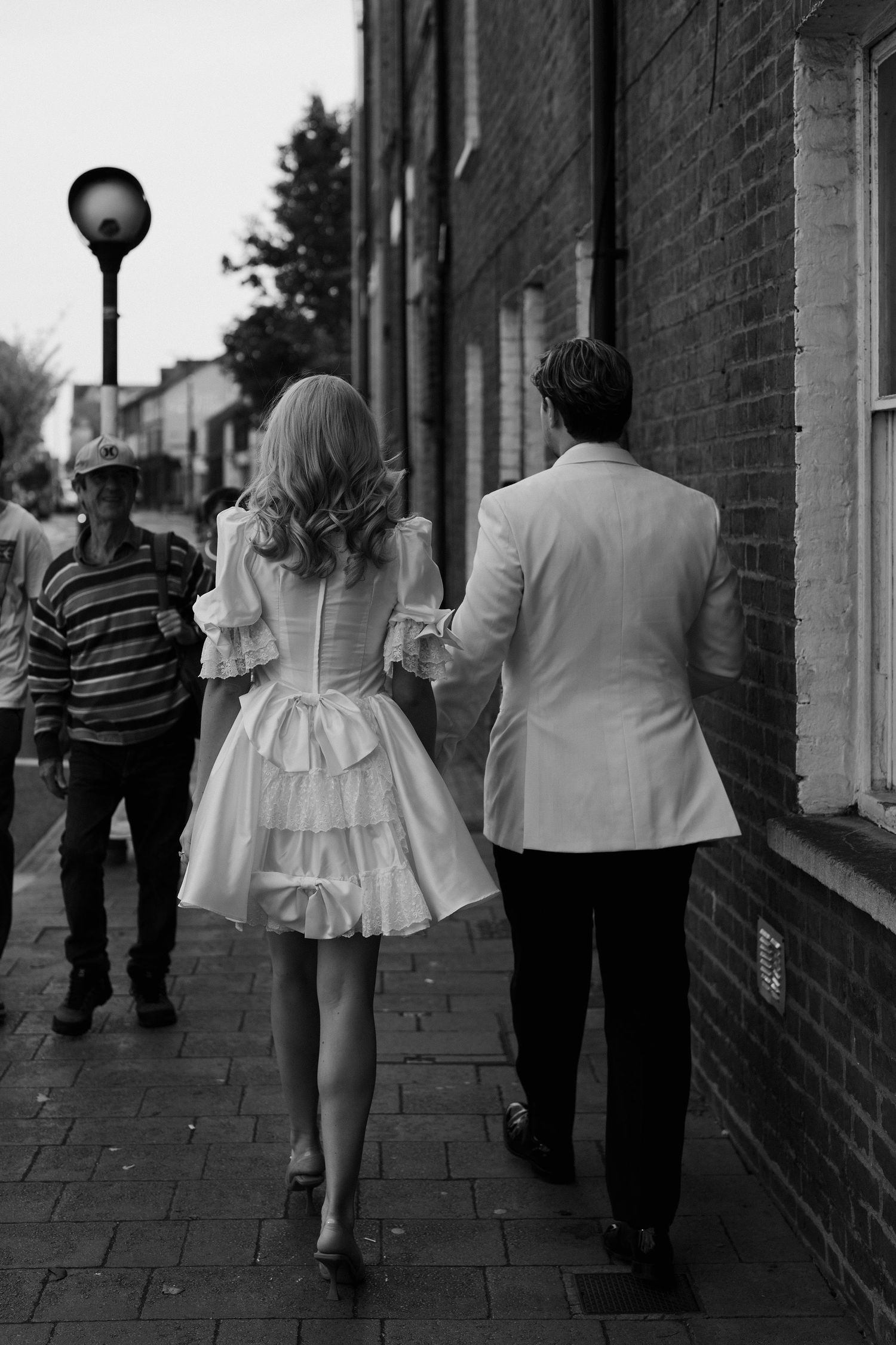 passerby smiling at bride and groom as they walk through oxford