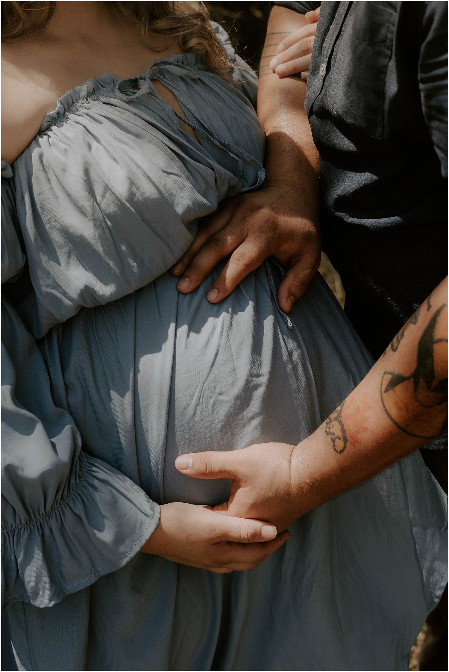 Close-up of hands tenderly placed on a flowy blue-gray dress with natural lighting and shadows.