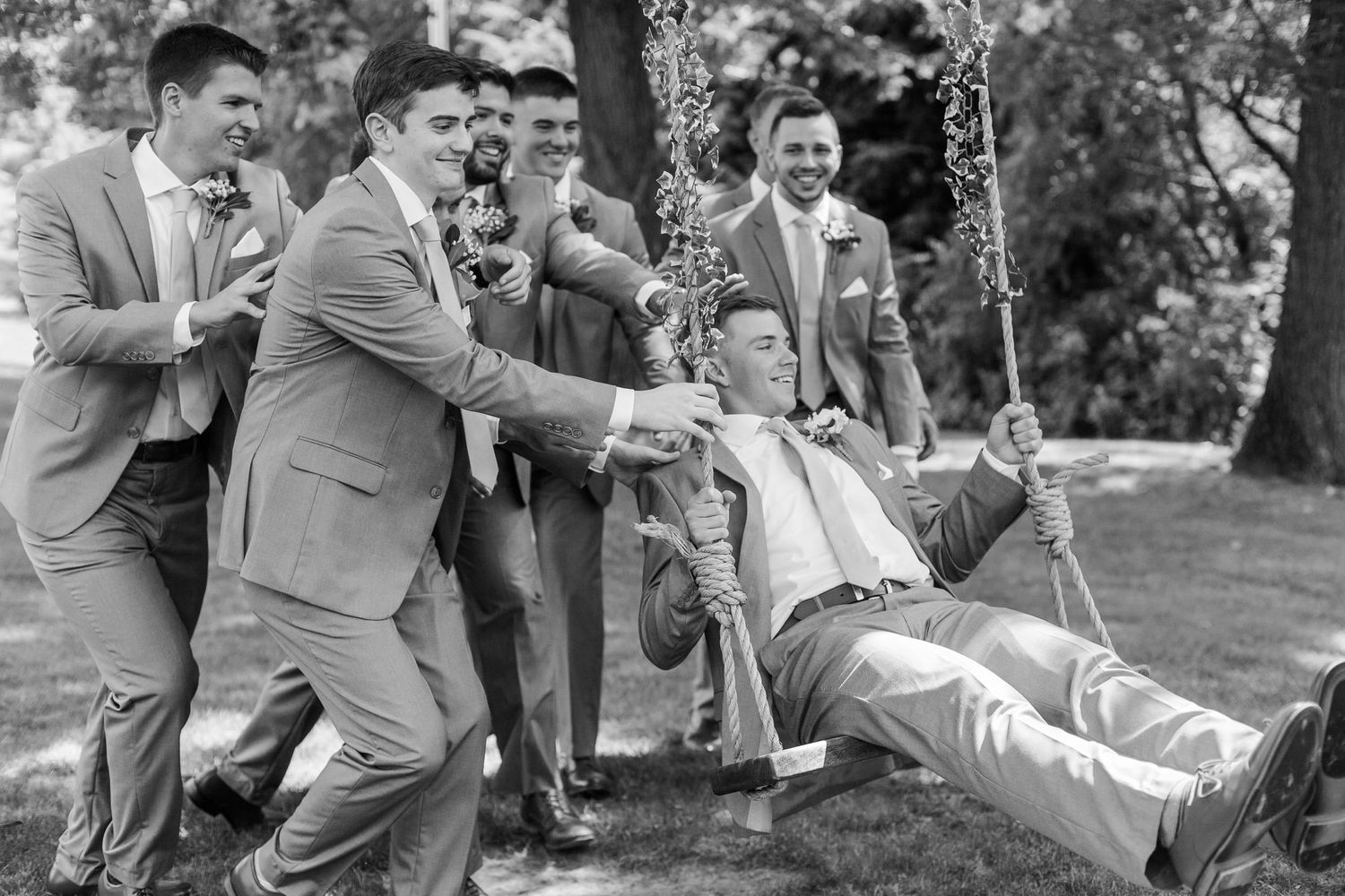 Groomsmen in gray suits perform playful poses in an outdoor setting.