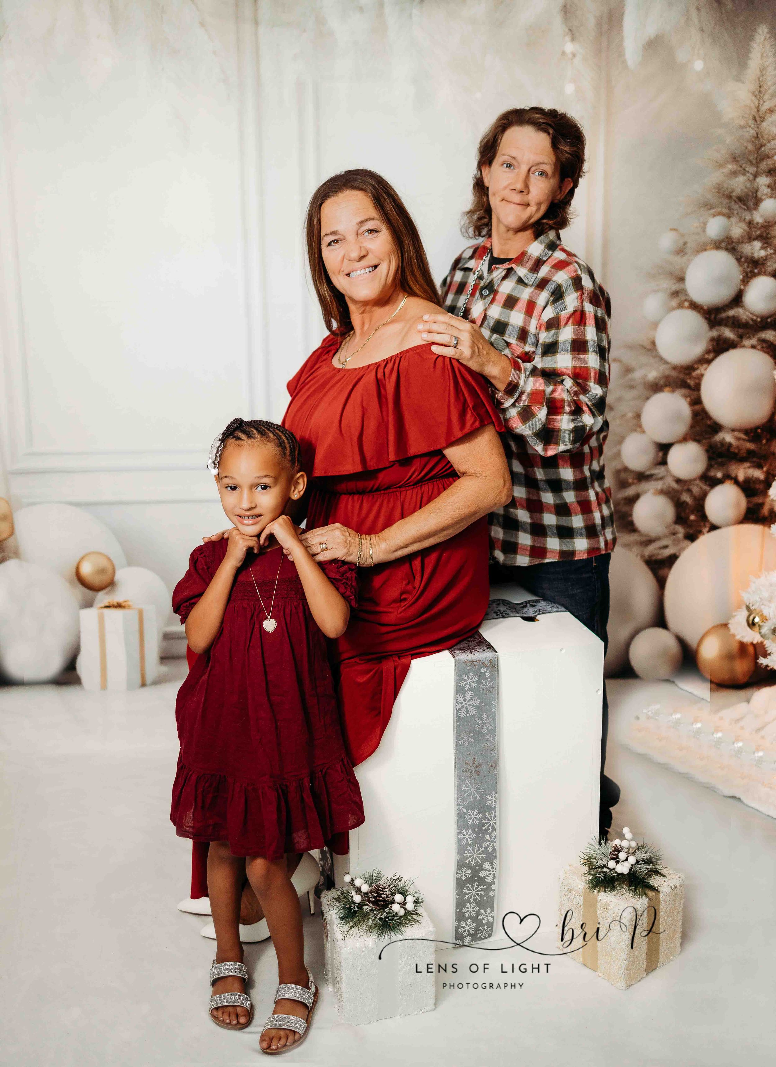 A family poses in front of a winter holiday backdrop with silver ornaments and wrapped presents.