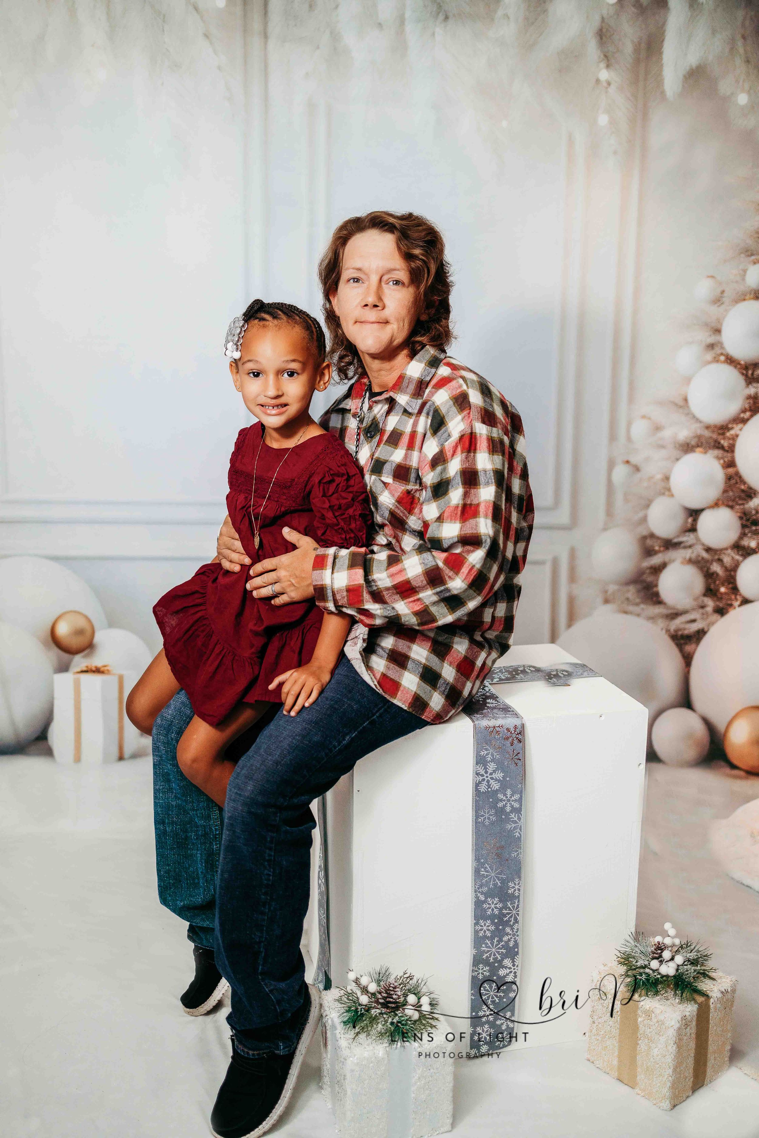 A holiday portrait in front of a winter backdrop with silver ornaments and wrapped presents.
