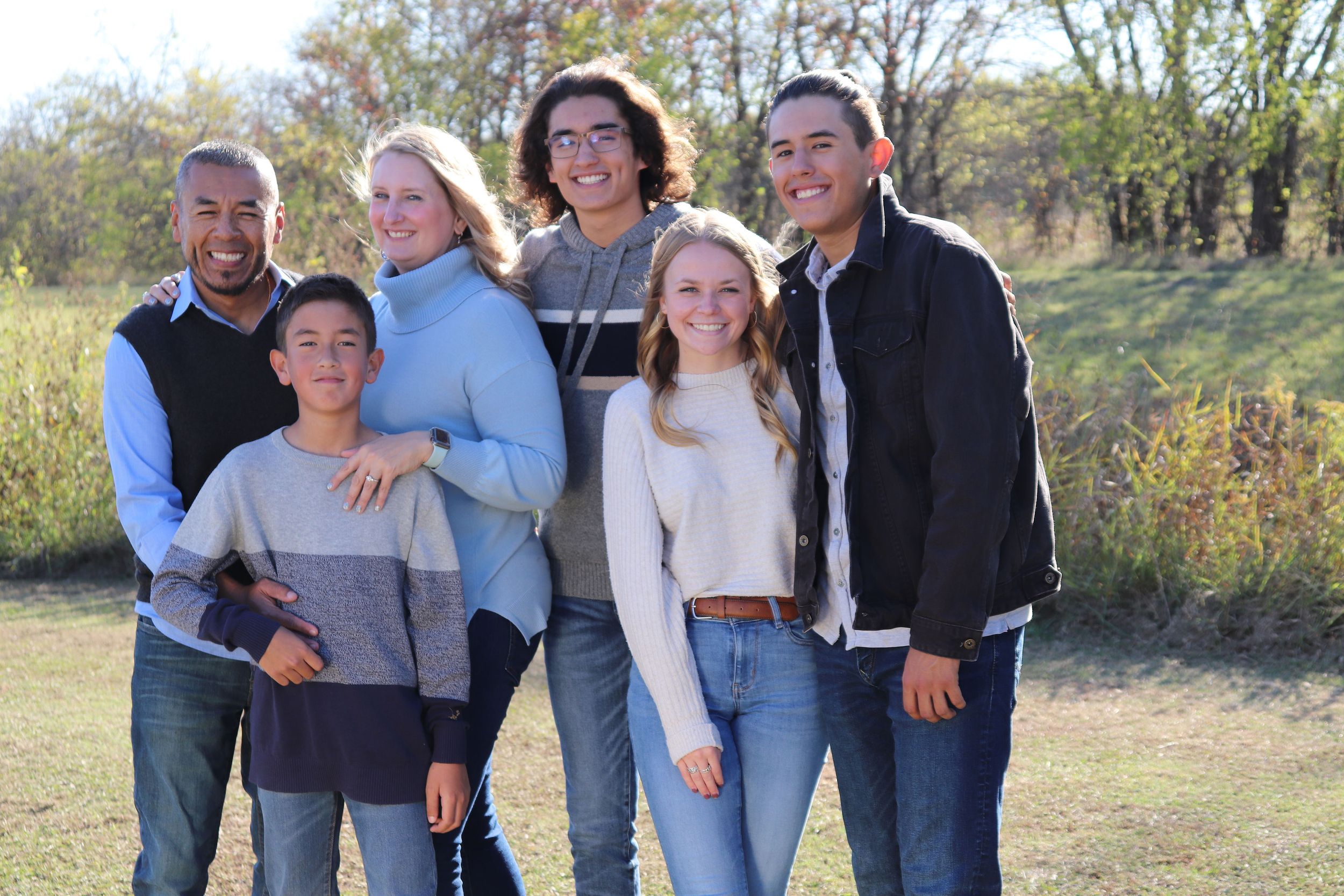 Blended family poses together for outdoor portrait in autumn setting.