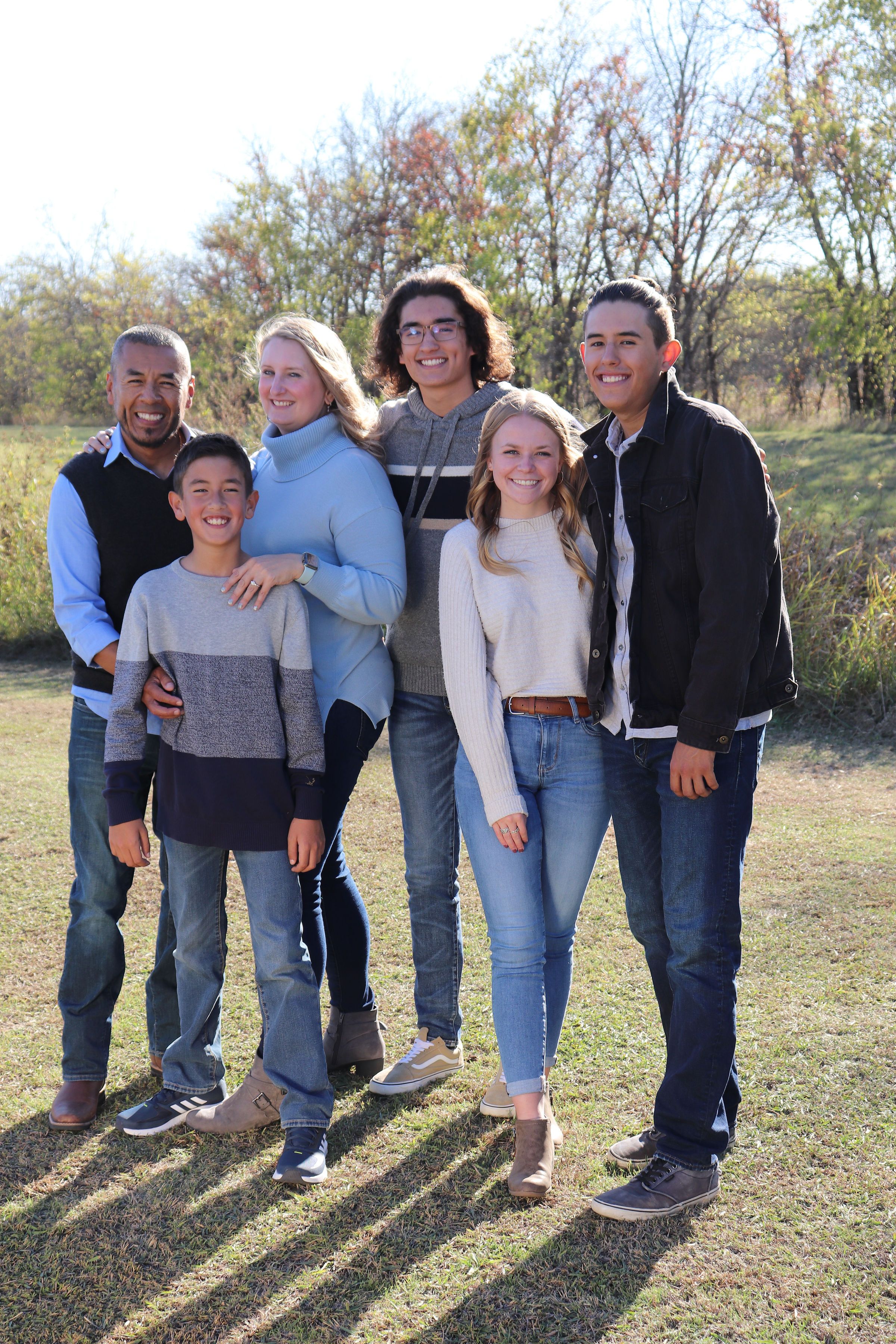 Group portrait of family members standing together in sunny field.