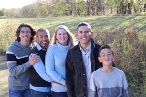 Family group poses together outdoors with autumn trees in background.
