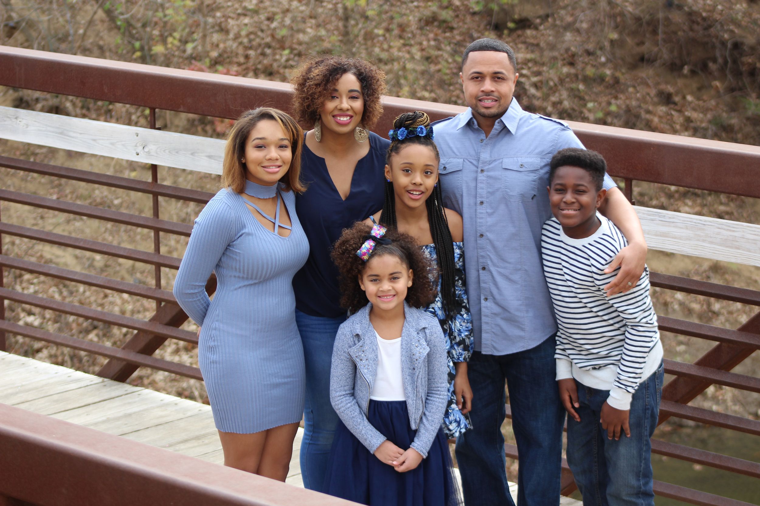 Family stands together on wooden bridge for portrait.
