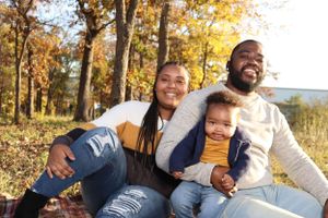 Happy family sitting together outdoors against fall foliage background.