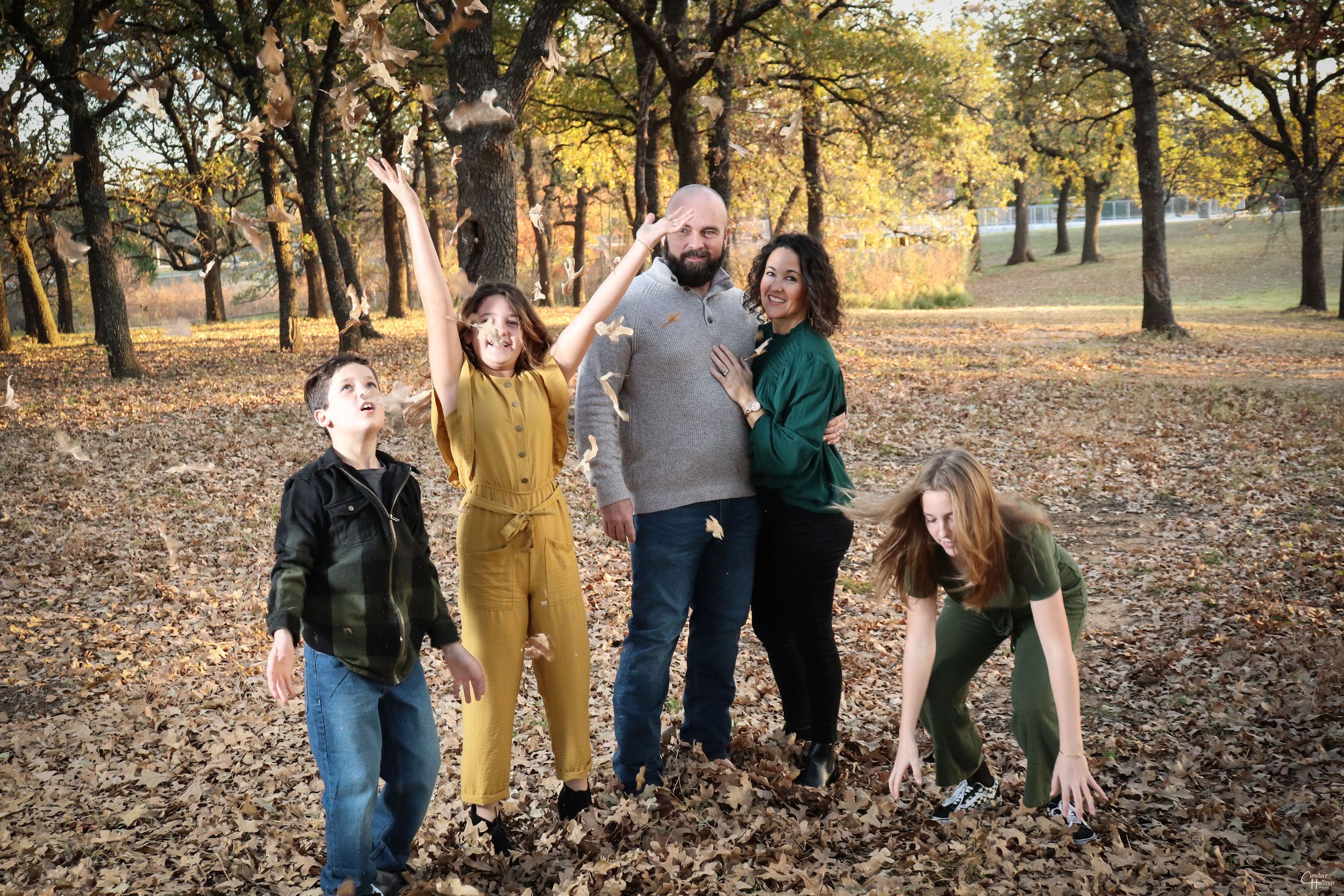 A playful group enjoying autumn foliage while posing together on fallen leaves in a wooded park setting.