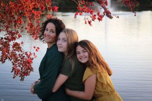 Three people in coordinating outfits pose together under vibrant red autumn leaves by a serene lake.