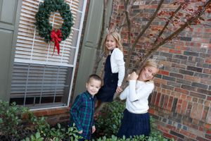 Children in uniforms pose near a brick house entrance decorated with a Christmas wreath.