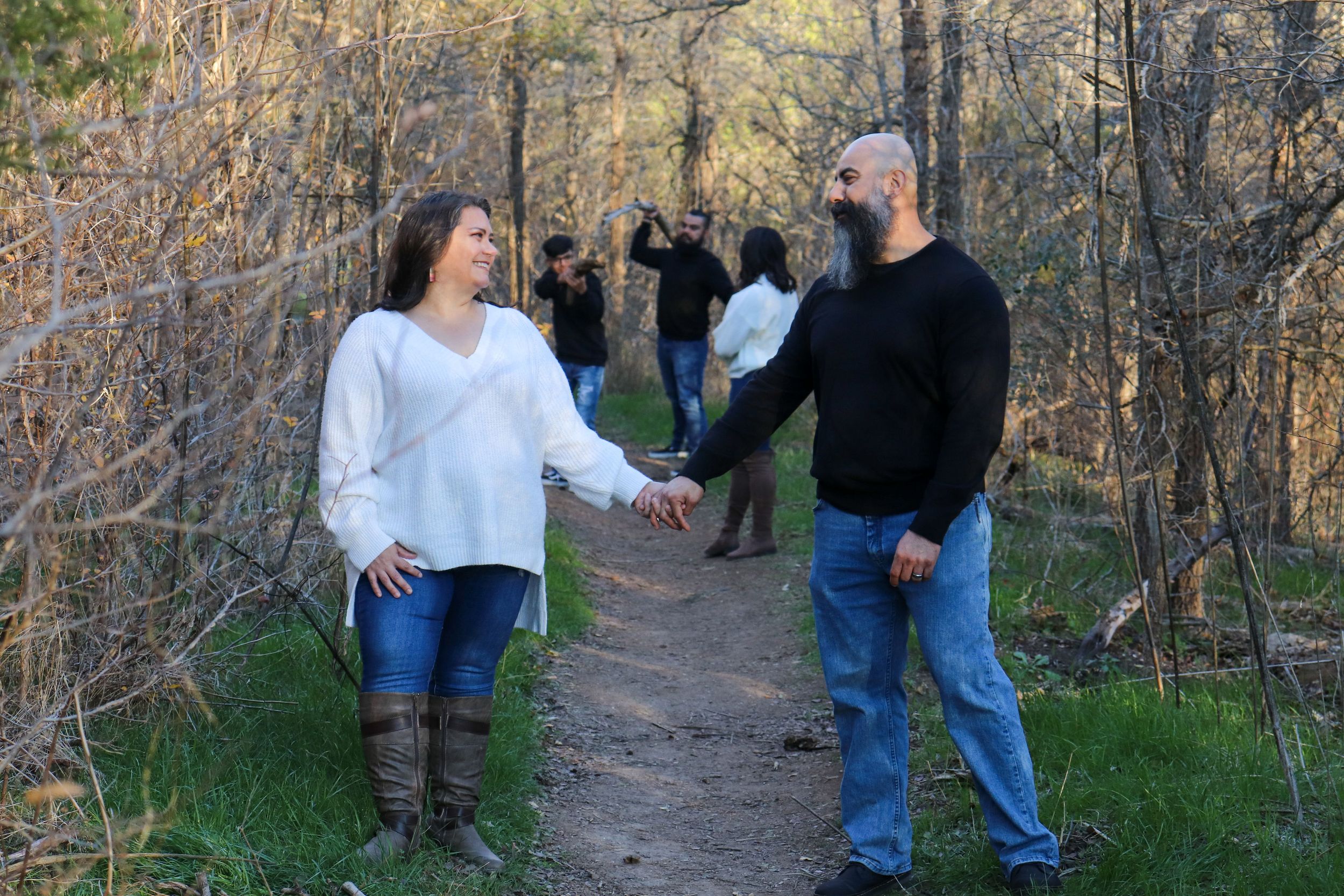 A couple holding hands while walking on a nature trail surrounded by autumn foliage.