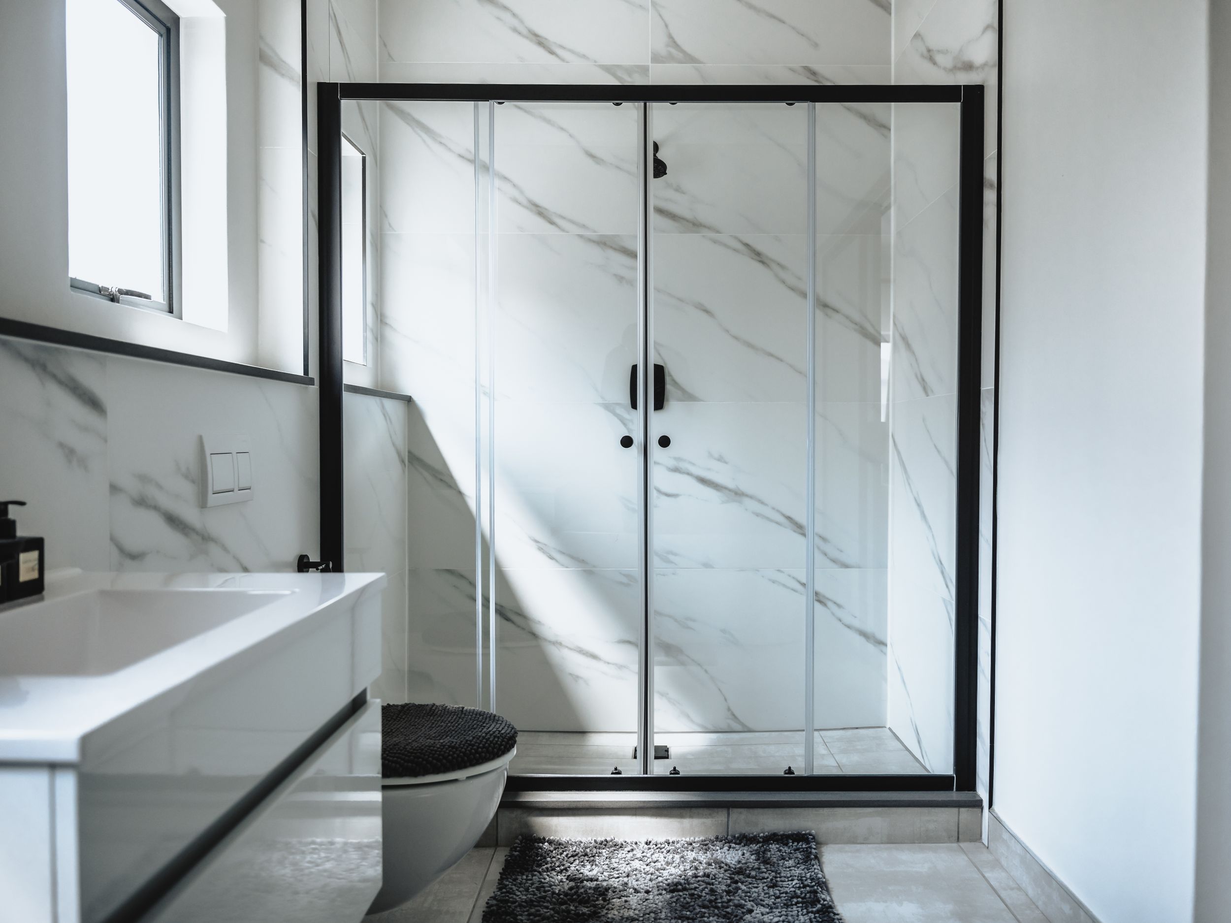 Elegant bathroom featuring marble walls, black framed shower doors and contemporary fixtures.