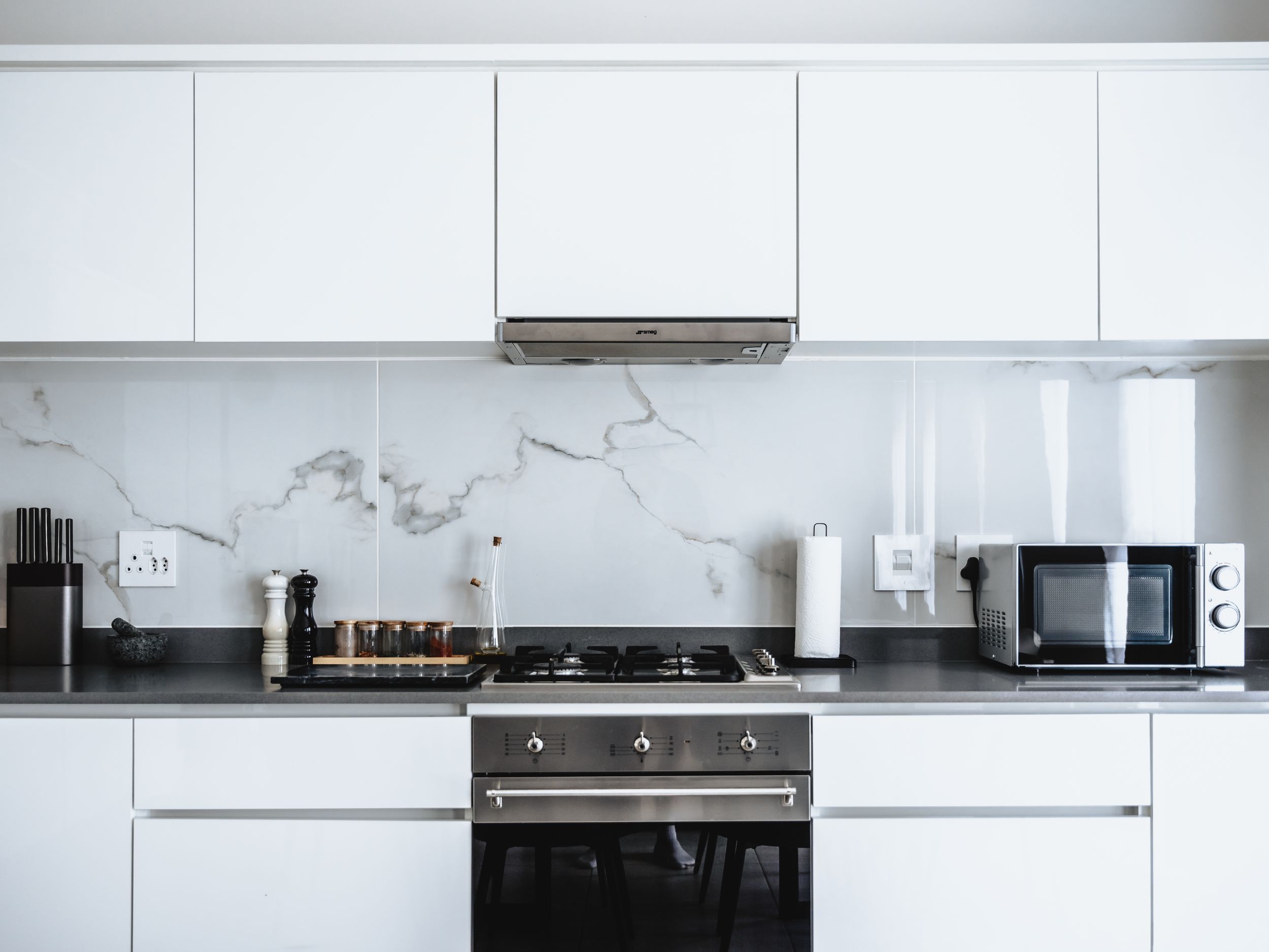 Sleek white modern kitchen with marble backsplash and black countertops featuring built-in appliances.