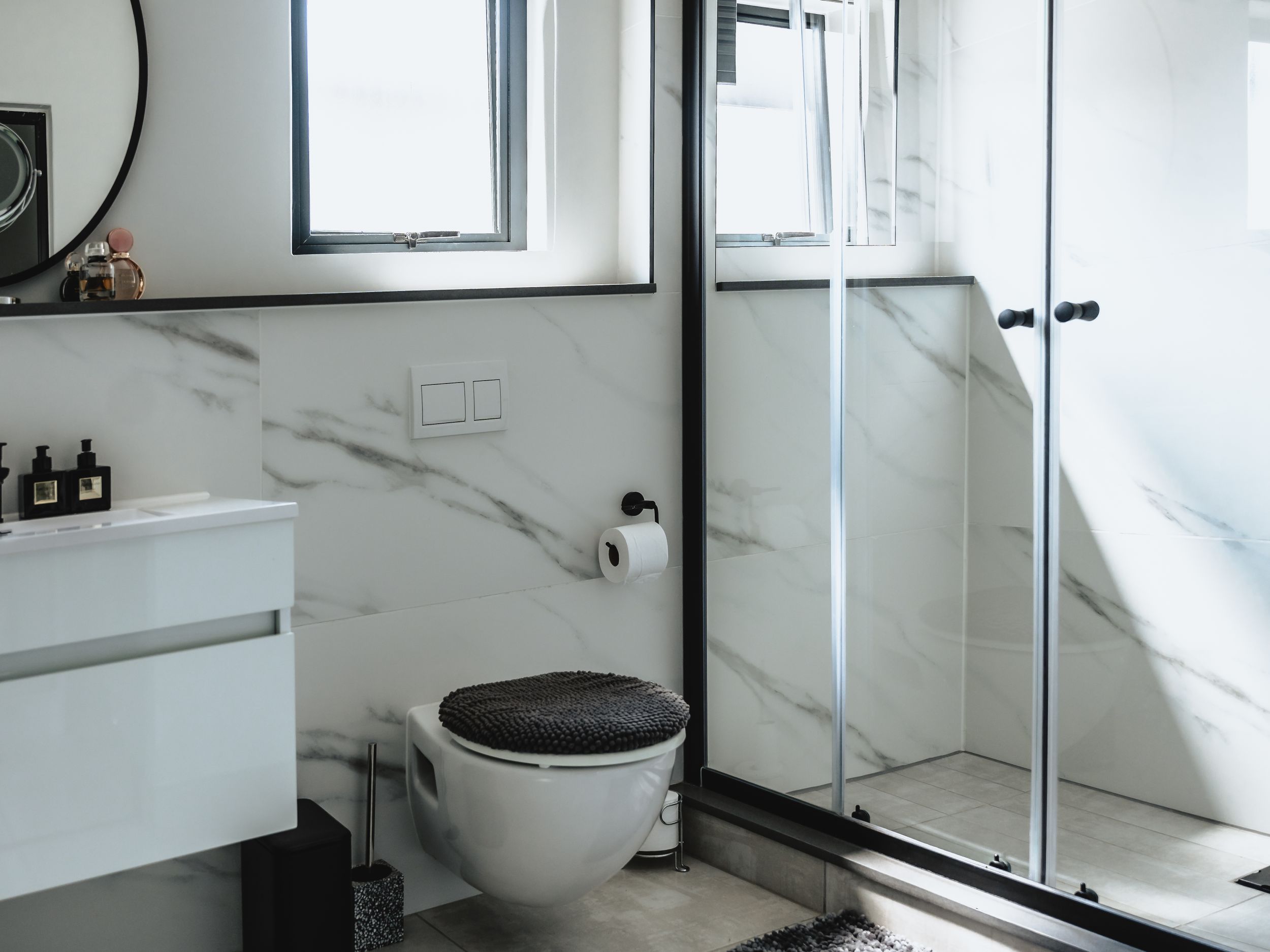 Modern bathroom with marble walls, glass shower enclosure and floating vanity in minimalist design.