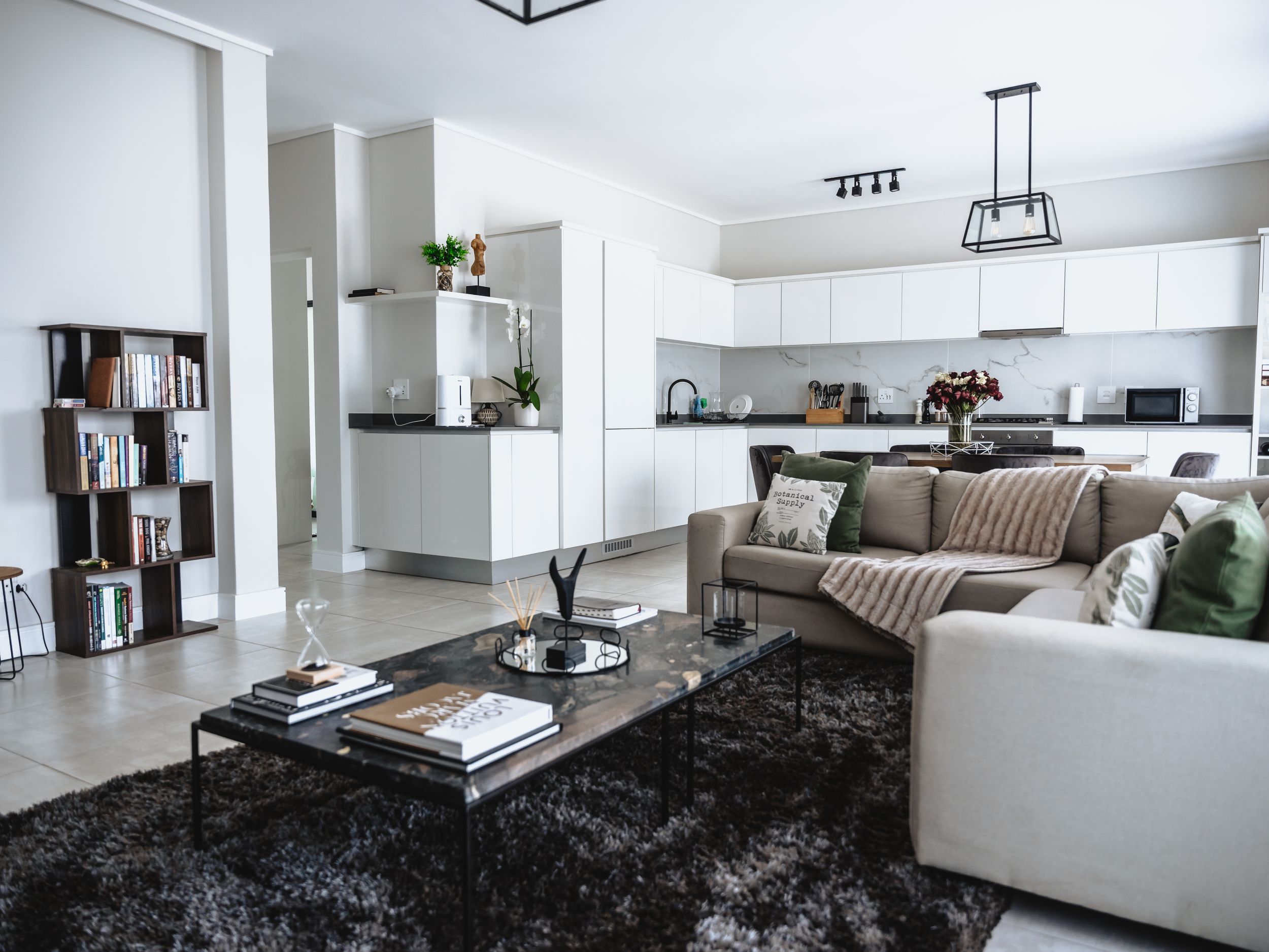 Modern open concept living room with black rug and white sectional sofa connecting to minimalist kitchen.