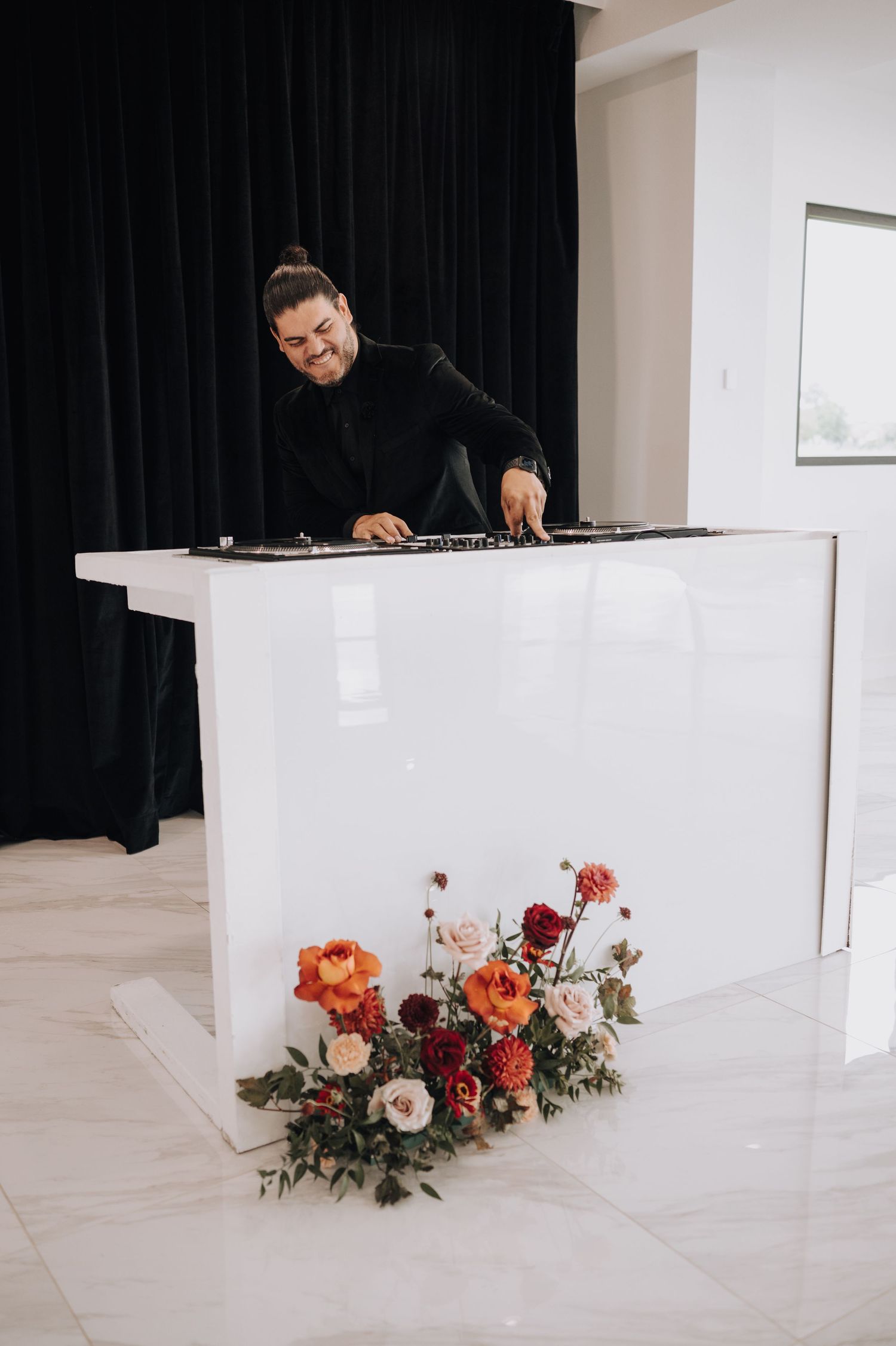Modern white DJ booth decorated with coral and cream floral arrangements against black curtain backdrop.