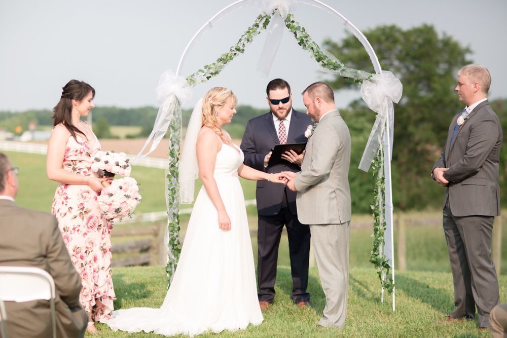 Outdoor wedding ceremony under floral arch with guests in attendance.