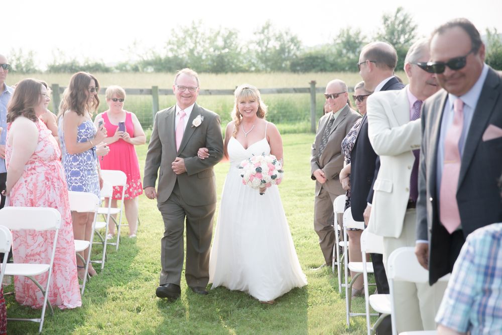 Wedding party walks down aisle on sunny day at outdoor rustic farm ceremony.