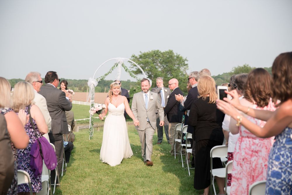 Wedding recessional down aisle with guests taking photos at outdoor farm ceremony.